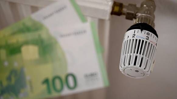Heizungsregler und unscharfer 100-Euro-Schein symbolisieren Energiekosten.