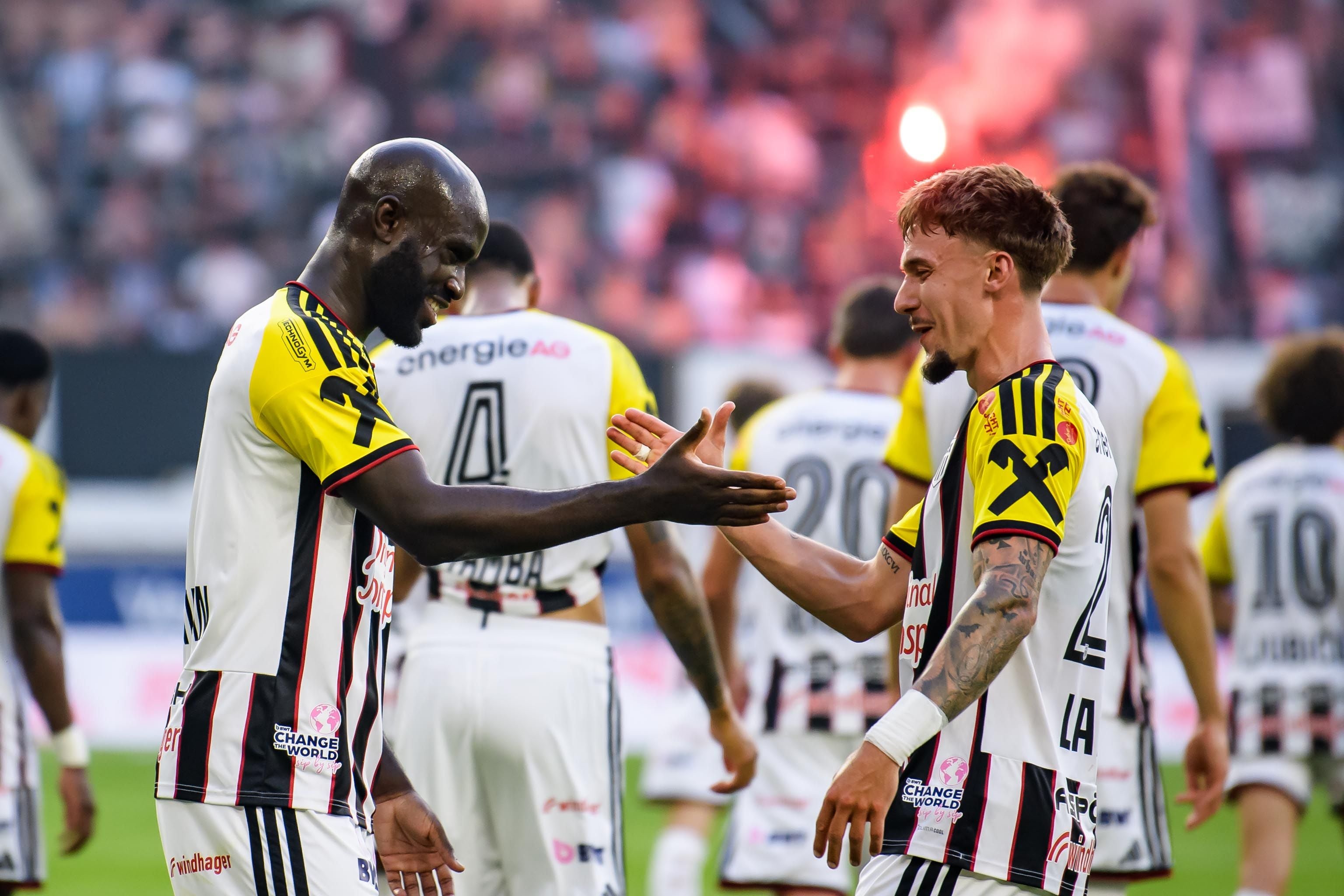 Zwei LASK-Spieler jubeln auf dem Fußballfeld und geben sich die Hand.