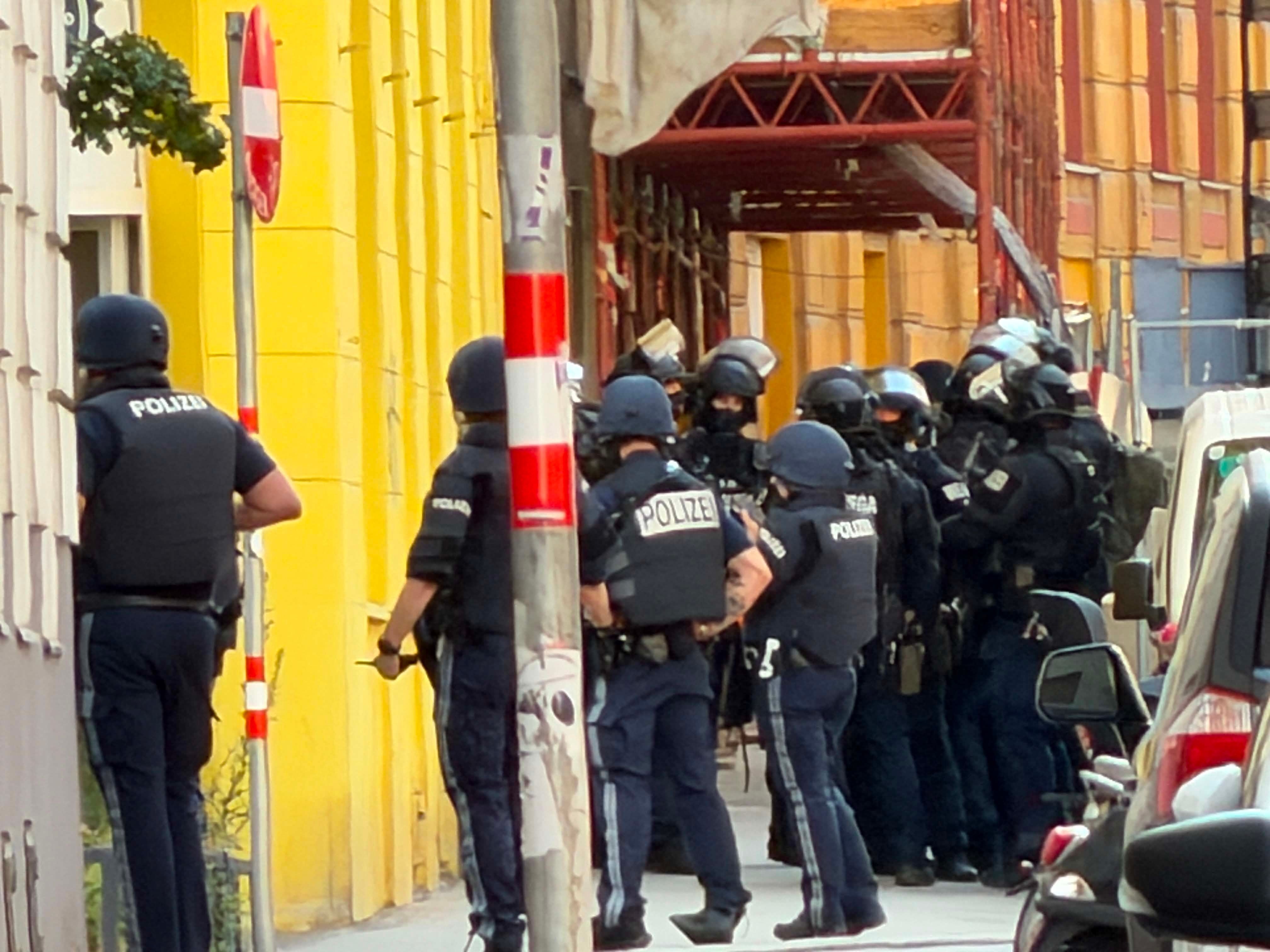Mehrere Polizisten in Schutzkleidung stehen vor einem gelben Gebäude in einer Stadtstraße.