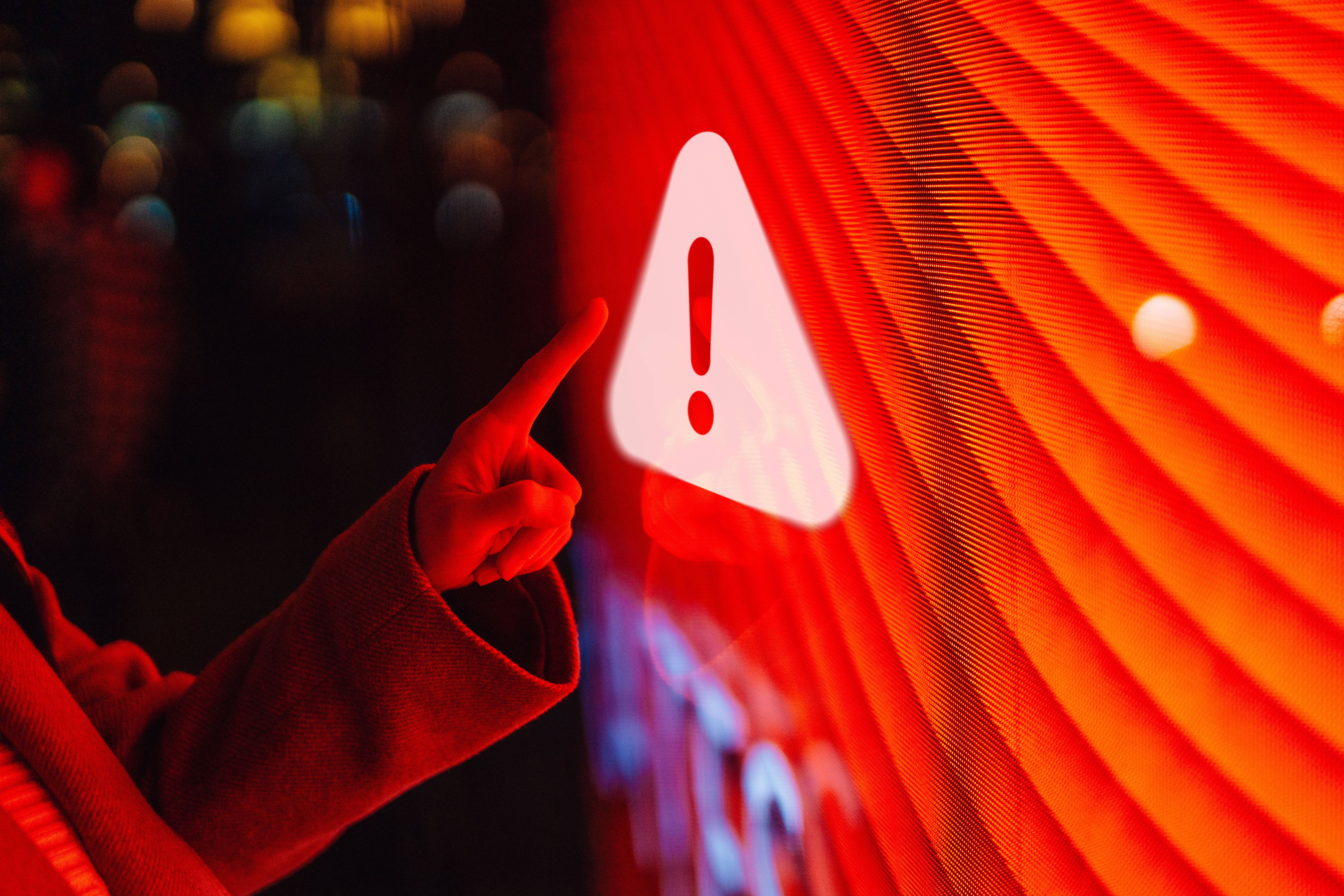 Finger zeigt auf rotes Warnsymbol mit Ausrufezeichen auf einem leuchtenden Bildschirm.