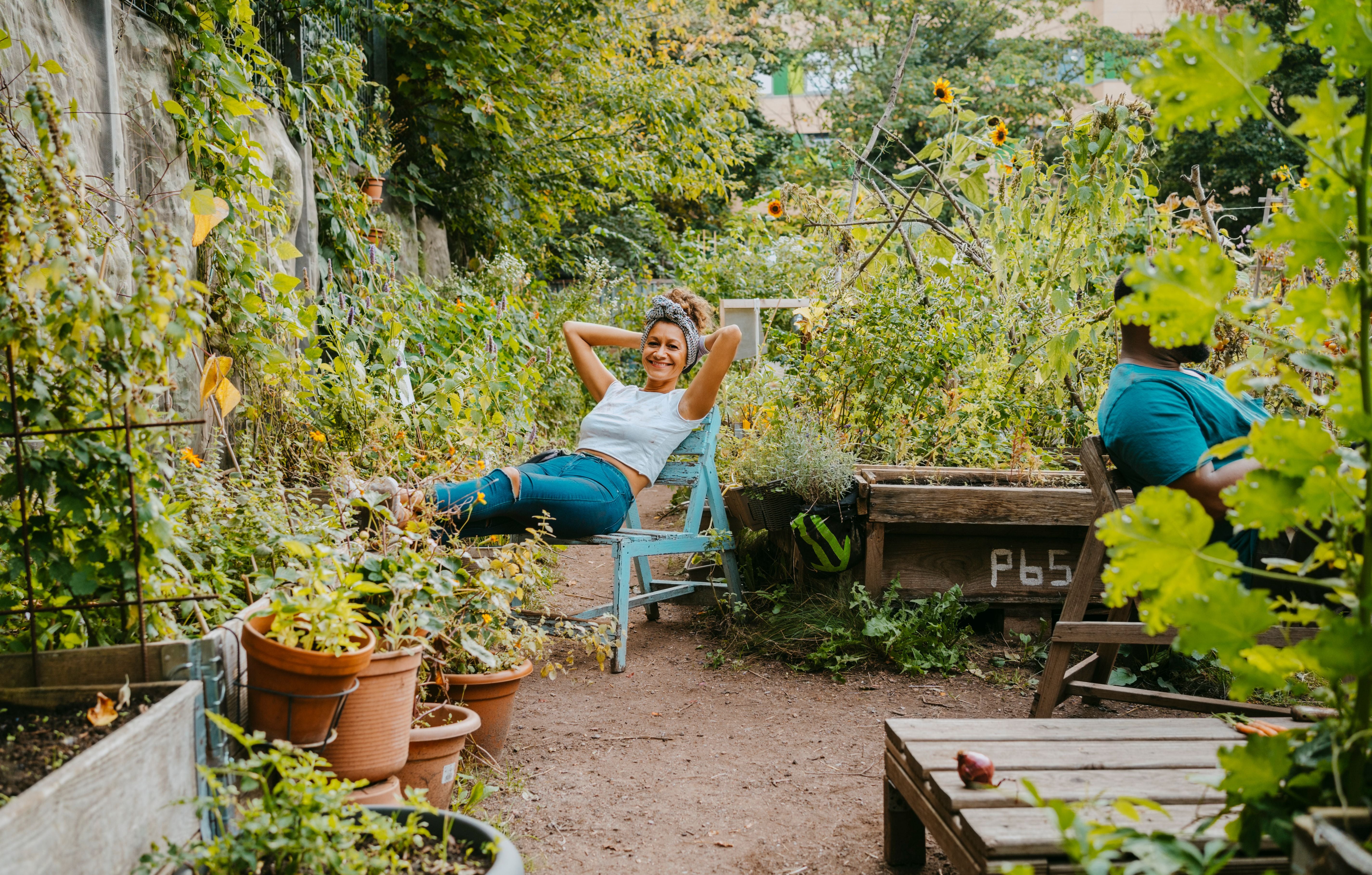 Eine Frau entspannt auf einem Stuhl in einem grünen, üppigen Gemeinschaftsgarten.