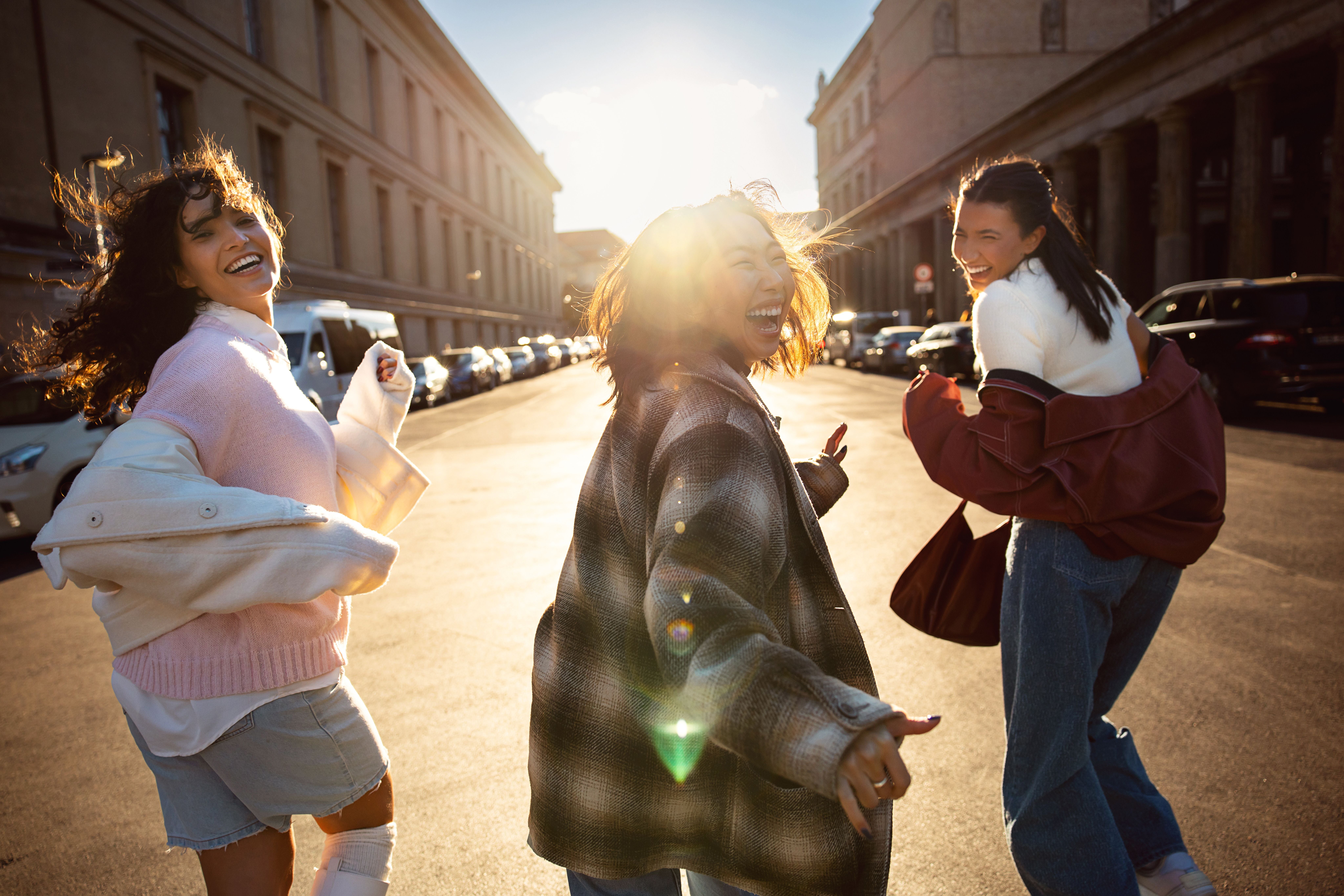 Drei junge Frauen lachen und laufen gemeinsam fröhlich durch eine sonnige Berliner Straße.