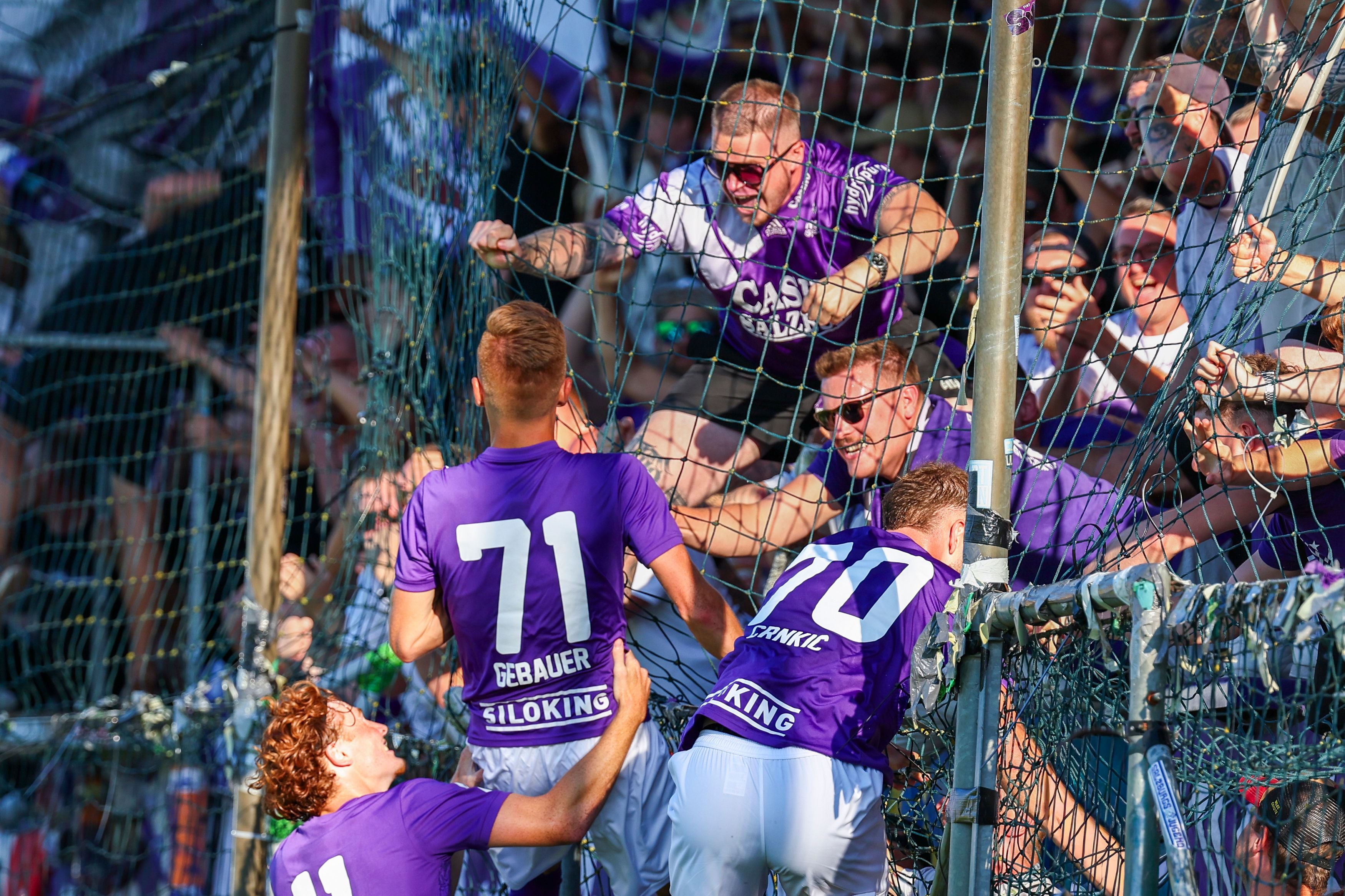 Jubelnde Austria Salzburg Spieler feiern mit Fans am Zaun nach einem Tor.