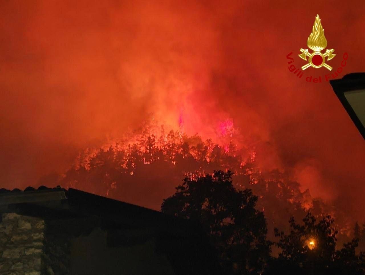 Ein großer Waldbrand am Gardasee mit dichtem Rauch und Flammen in der Nacht.
