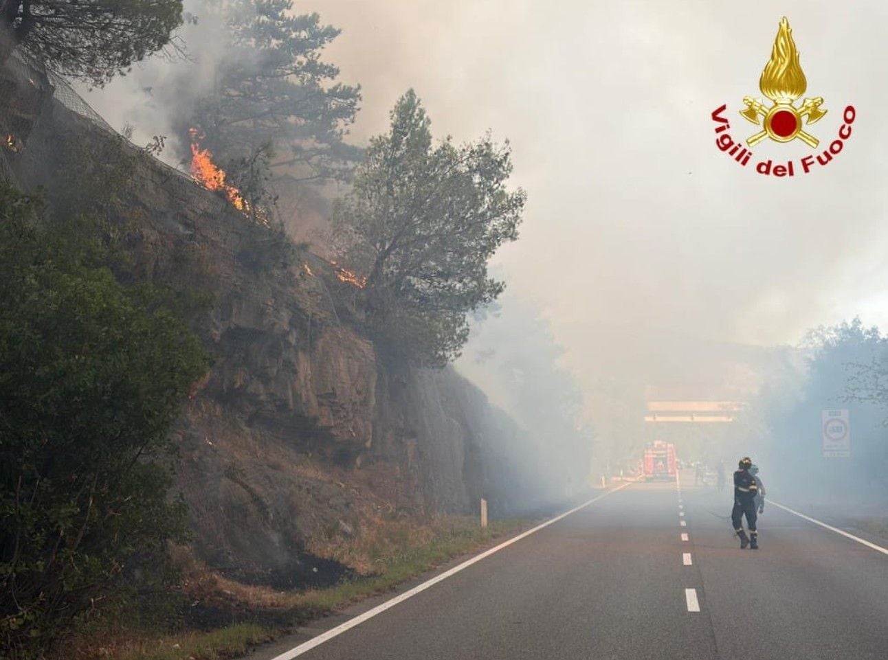 Feuerwehr bekämpft Waldbrand an einer rauchigen Straße in Norditalien.