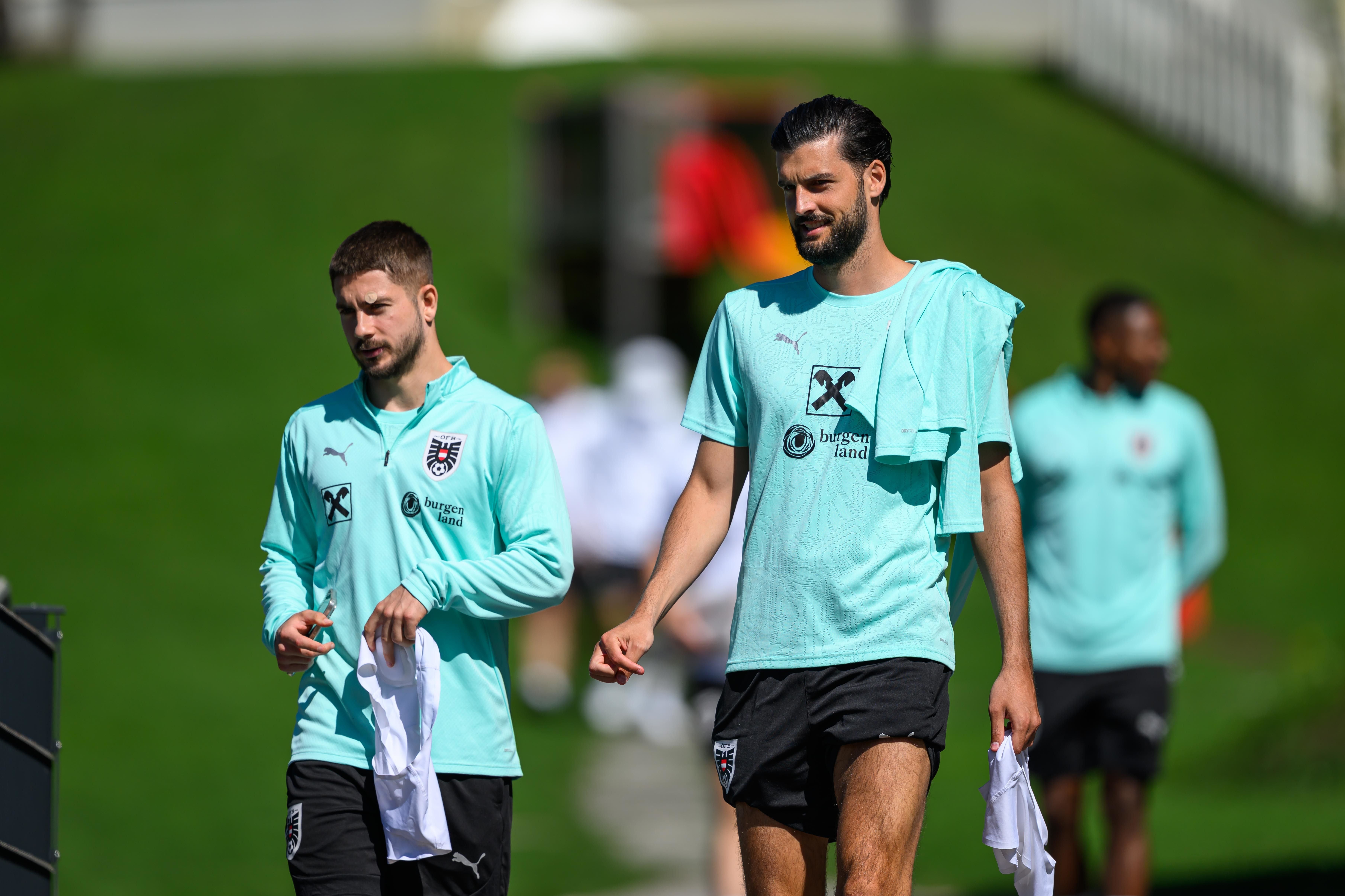 Zwei österreichische Fußballspieler im Trainingsanzug gehen nebeneinander auf einem Sportplatz.