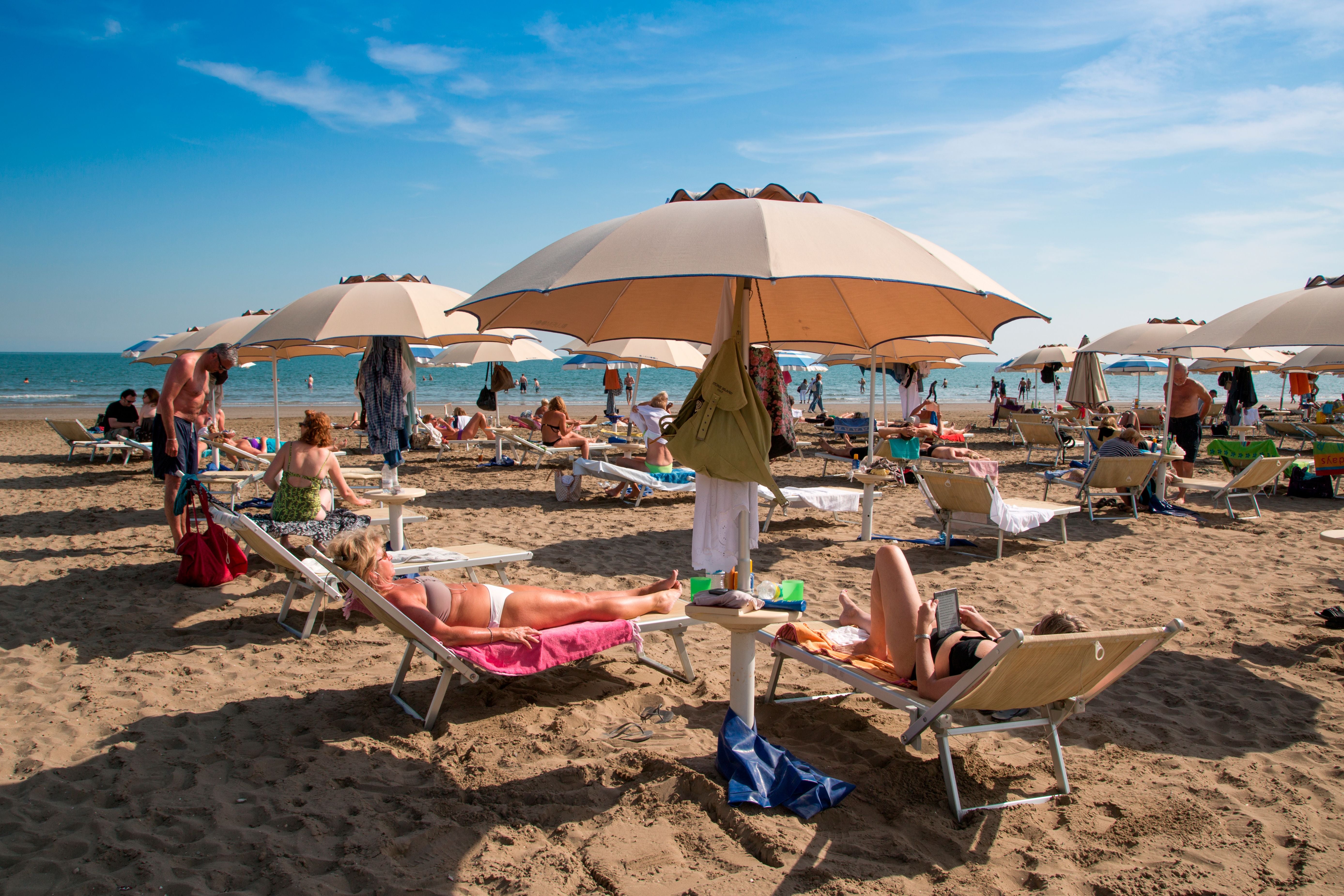 Menschen entspannen auf Liegestühlen unter Sonnenschirmen am Sandstrand eines belebten Strandes.