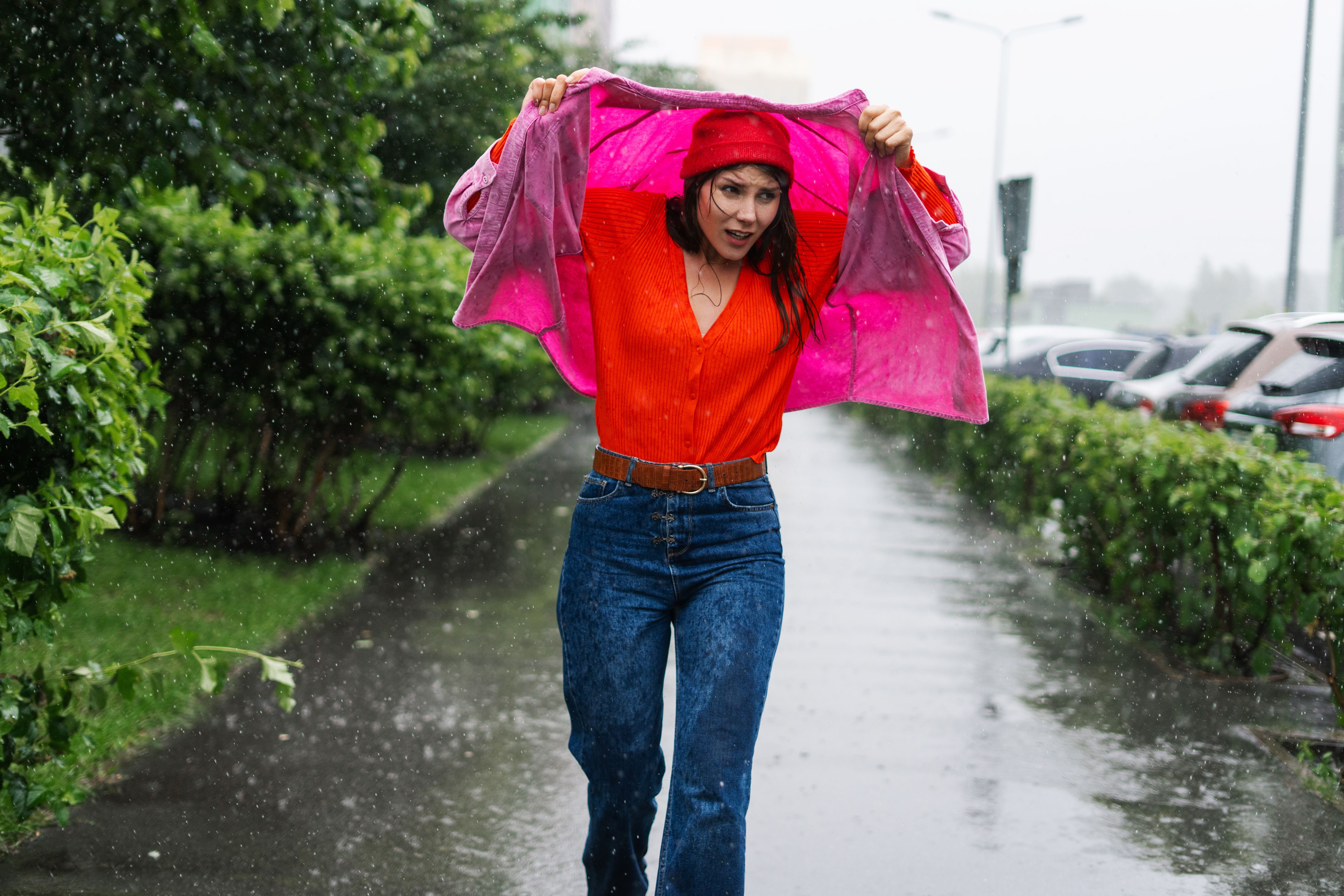 Frau läuft im Regen und schützt sich mit einer Jacke über dem Kopf auf nasser Straße.