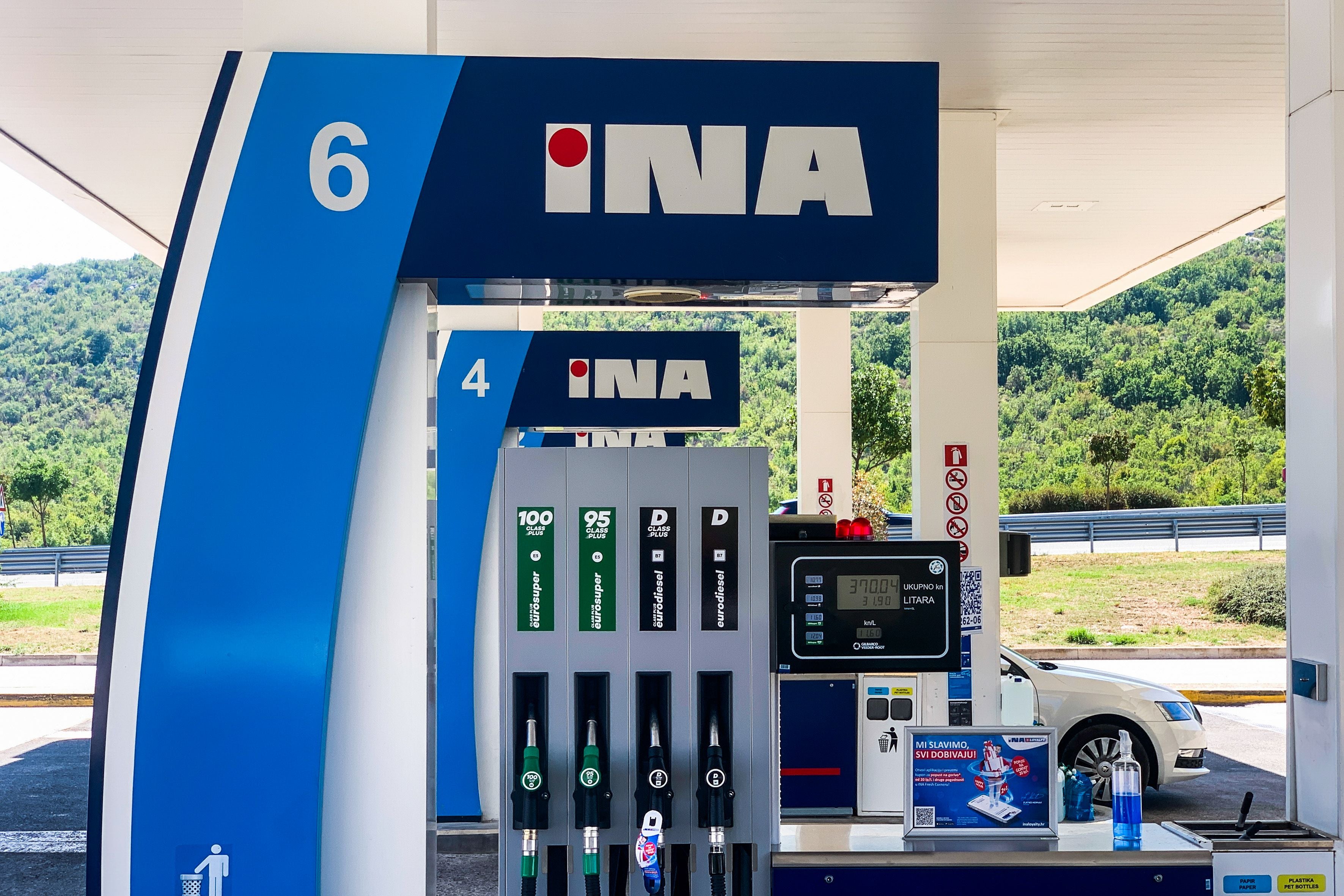 Zapfsäulen einer INA-Tankstelle in Blaca, Kroatien, mit Preisanzeige und Autotür im Hintergrund.