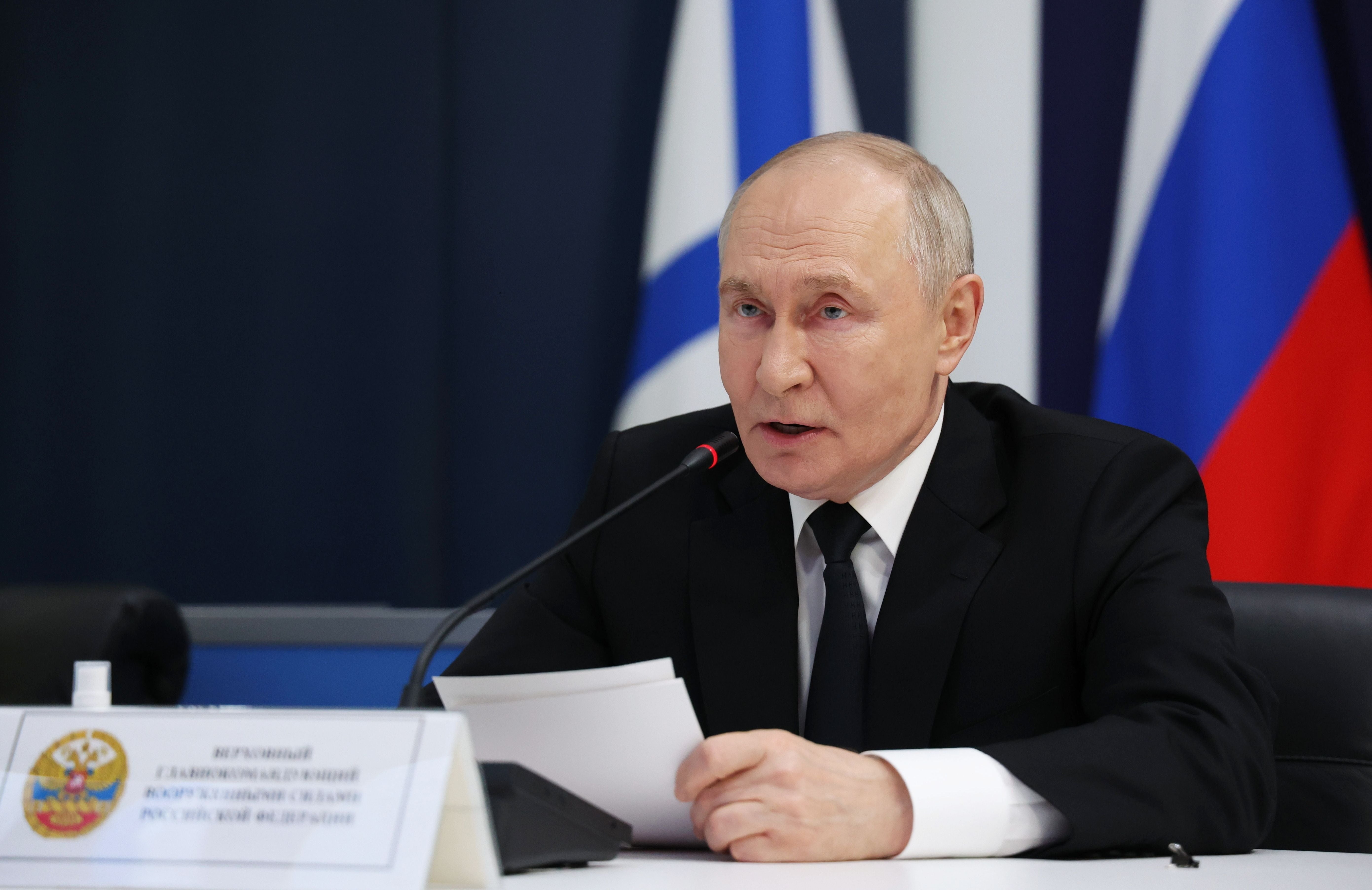 Ein Mann im Anzug spricht bei einer Konferenz mit Mikrofon und russischer Flagge im Hintergrund.