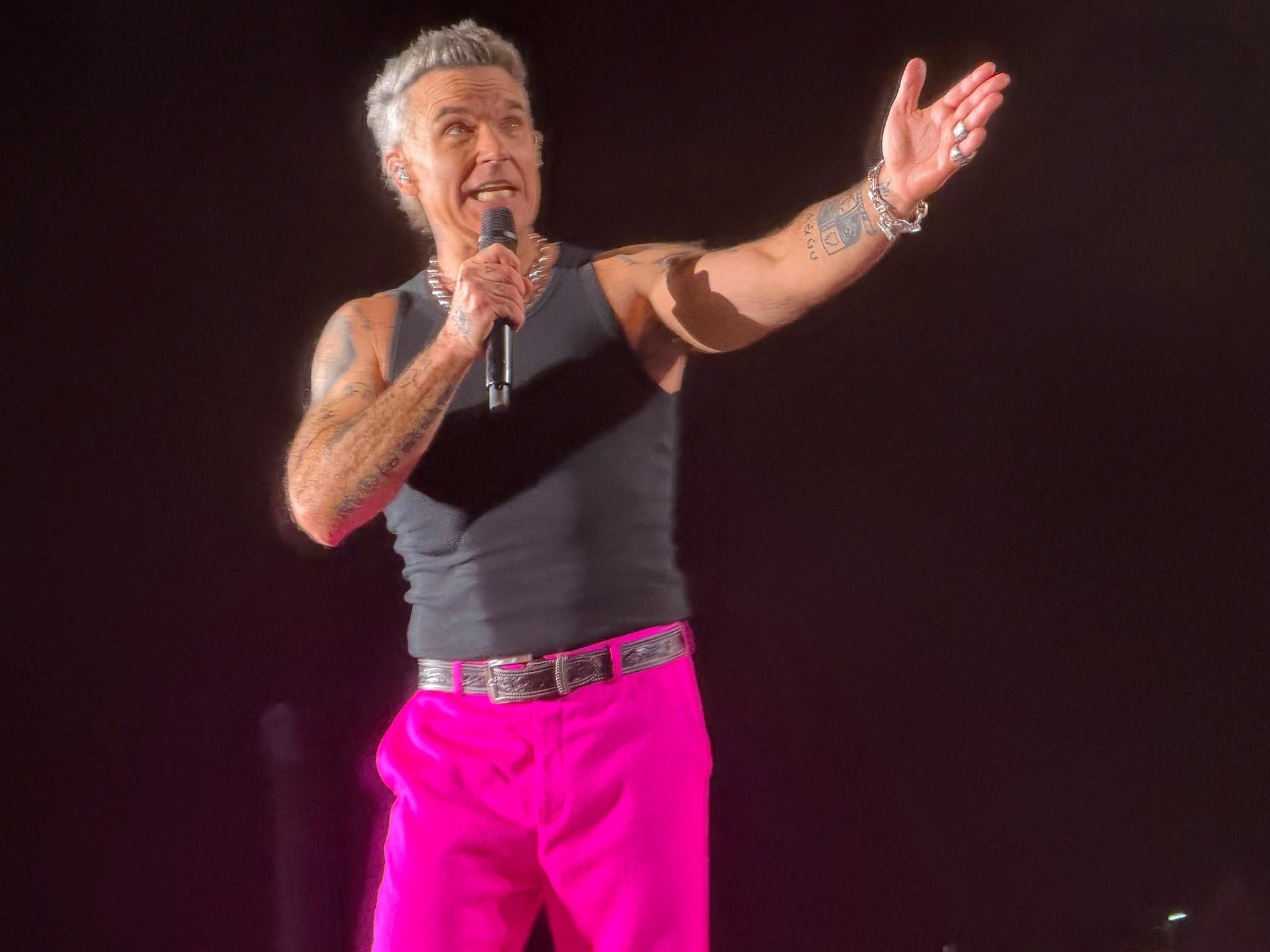Sänger mit Mikrofon trägt schwarzes Tanktop und pinke Hose auf der Bühne.