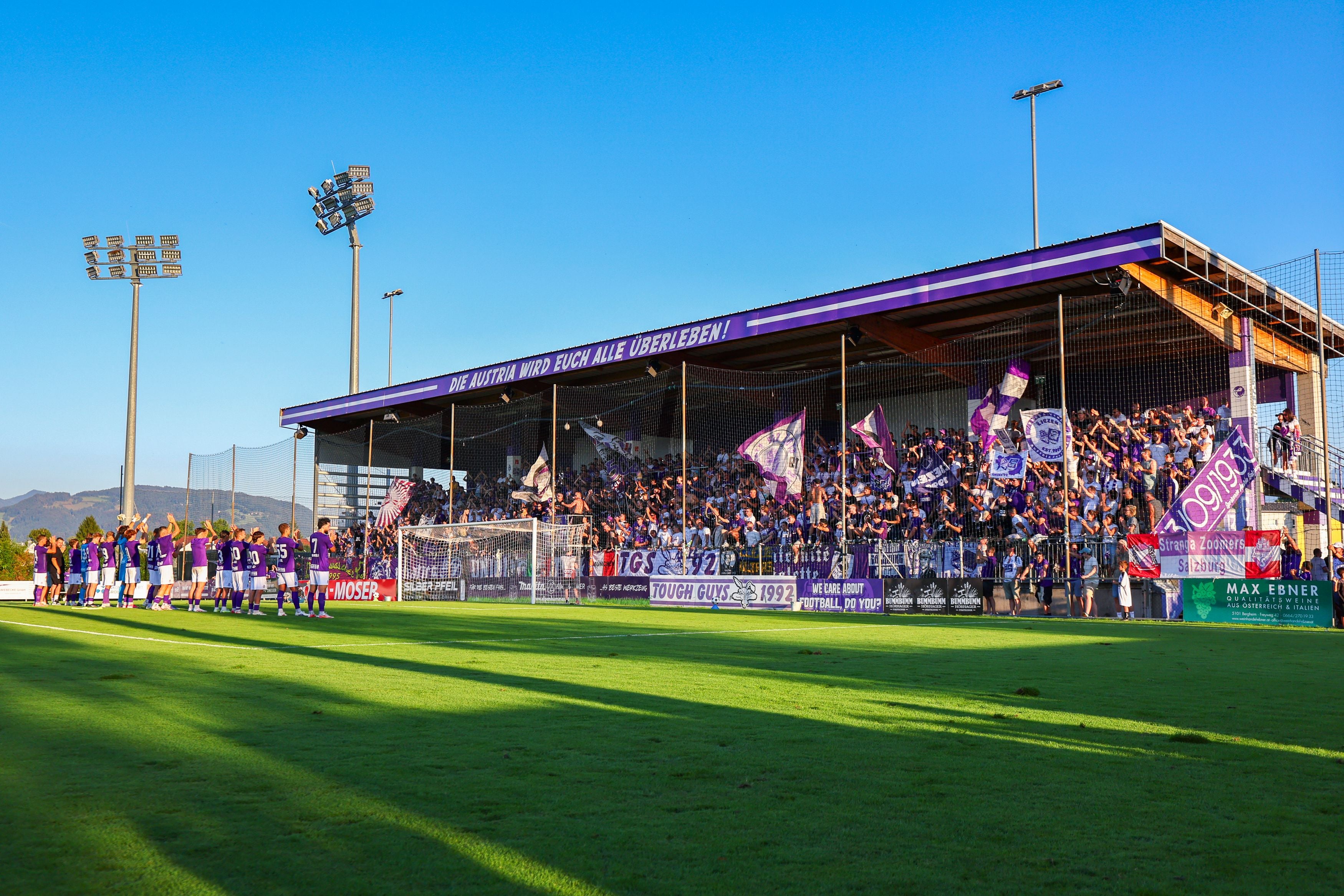Spieler von Austria Salzburg feiern mit ihren Fans vor einer vollen, violetten Tribüne im Stadion.