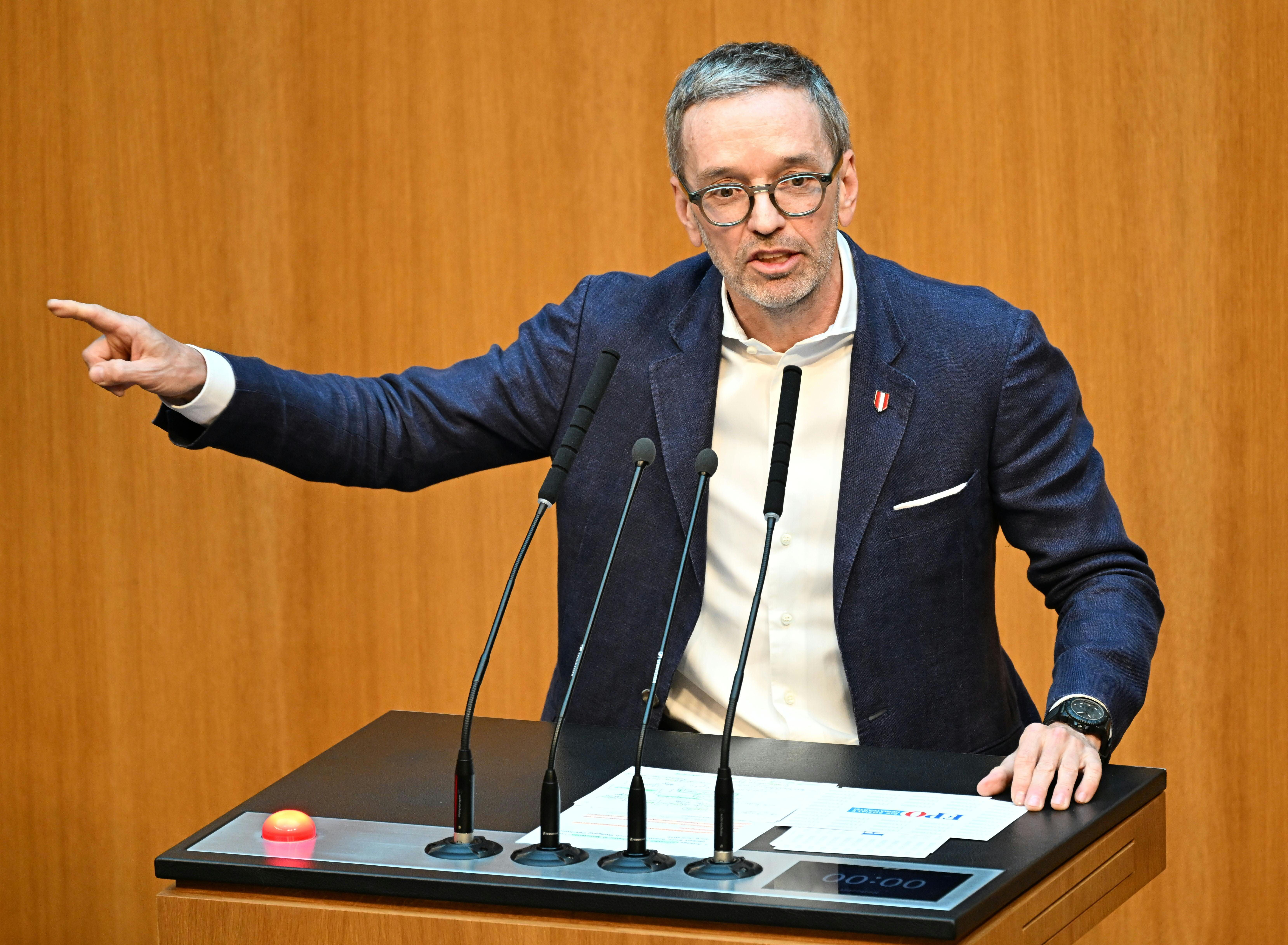 Ein Mann im blauen Sakko spricht am Rednerpult und gestikuliert mit der linken Hand nach links.