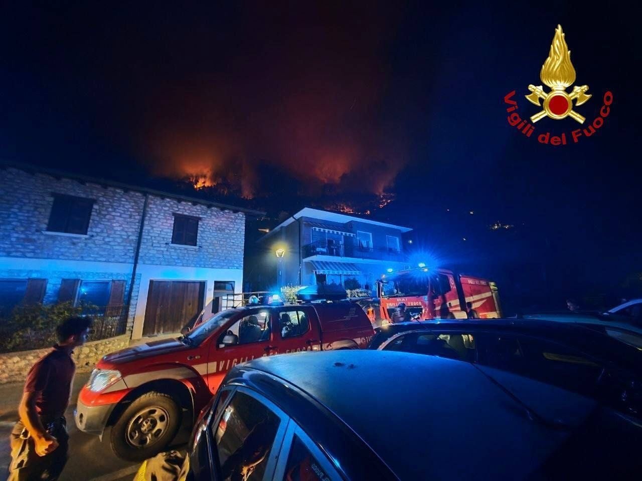 Waldbrandam Gardasee bei Nacht, Feuerwehrfahrzeuge und Einsatzkräfte vor Wohnhäusern.