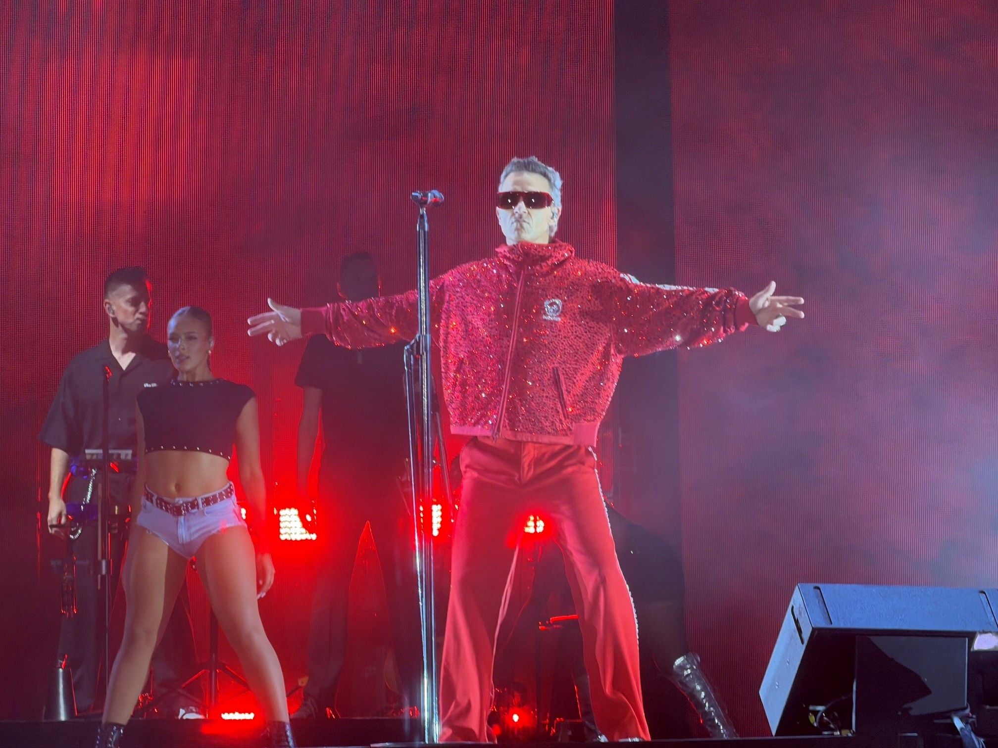 Robbie Williams auf einer Bühne in Bratislava mit Tänzern und roter Beleuchtung.