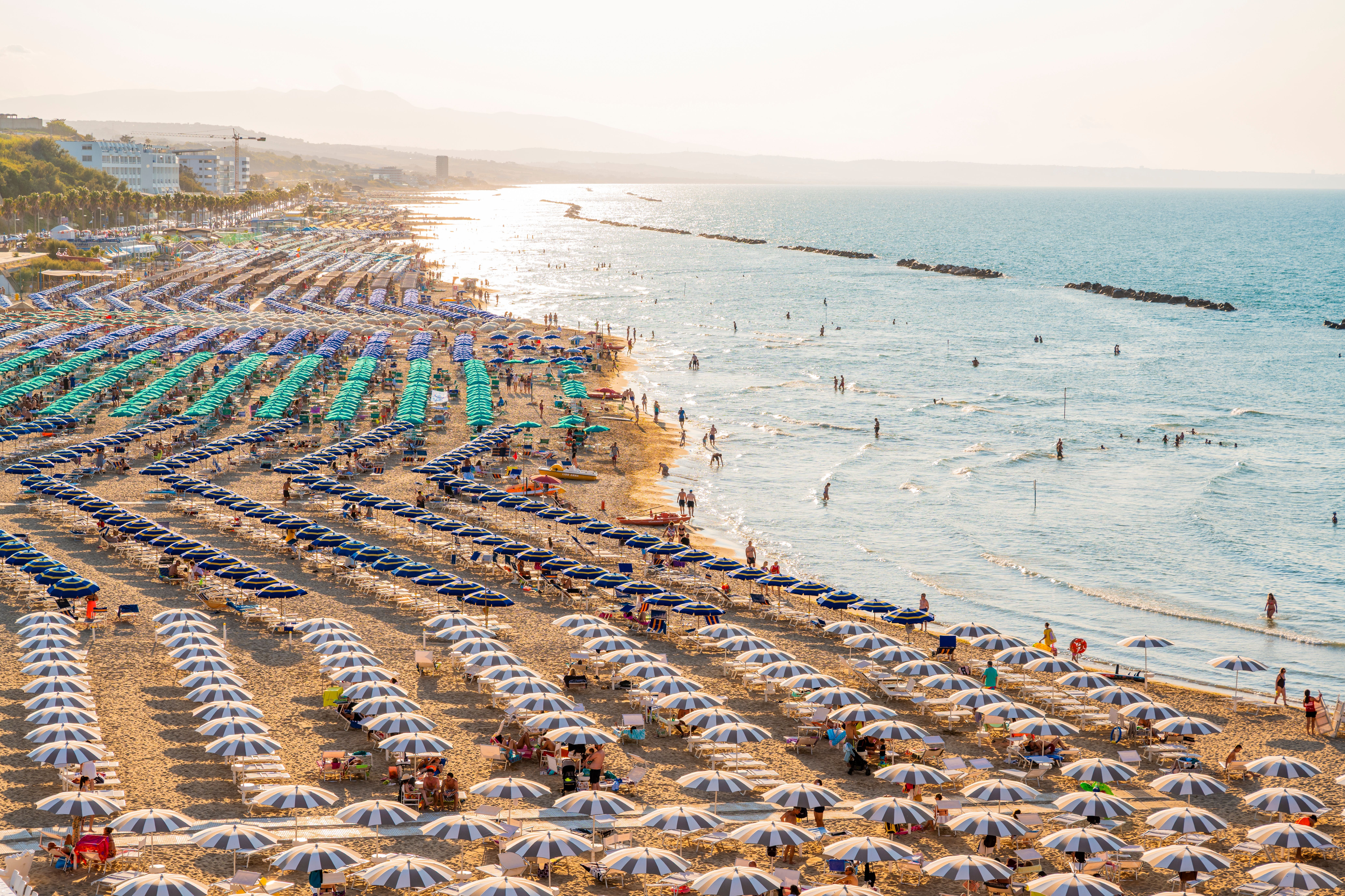 Luftaufnahme eines vollen Strandes in Termoli mit hunderten gestreiften Sonnenschirmen am Meer.