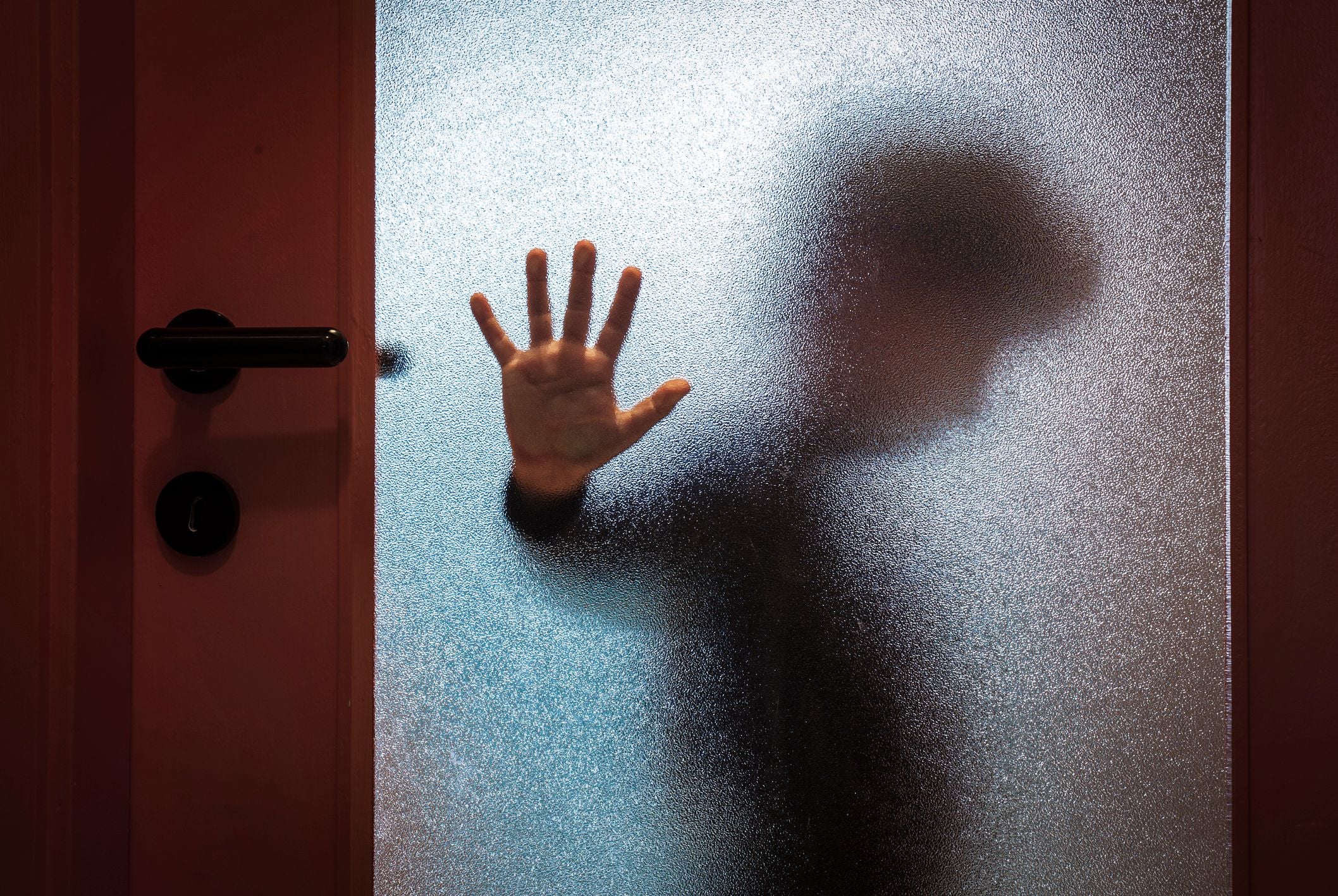 Verschwommener Junge drückt seine Hand gegen eine Glas­tür und wirkt traurig.