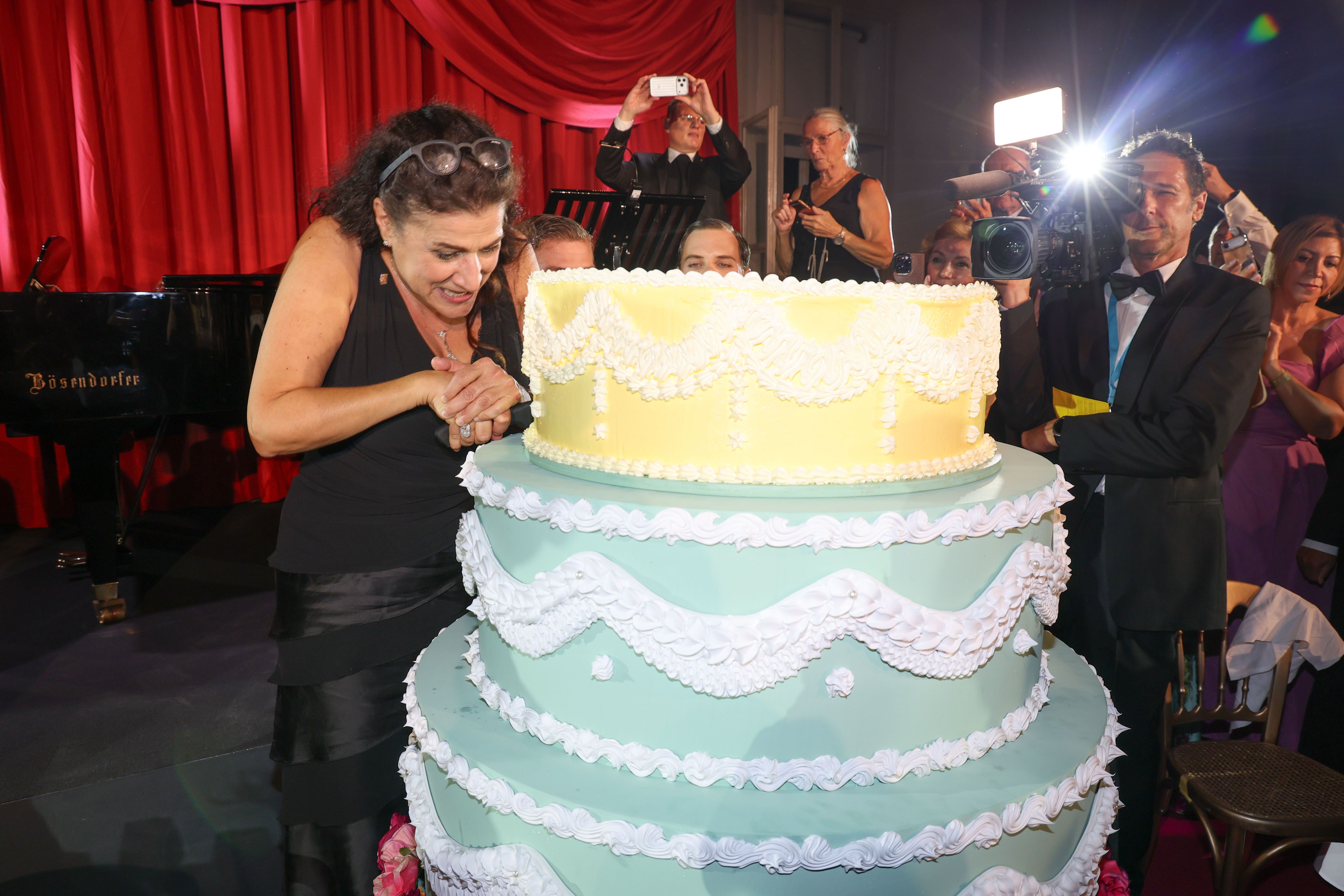 Cecilia Bartoli schneidet eine große, festliche Torte bei einer Gala-Veranstaltung an.