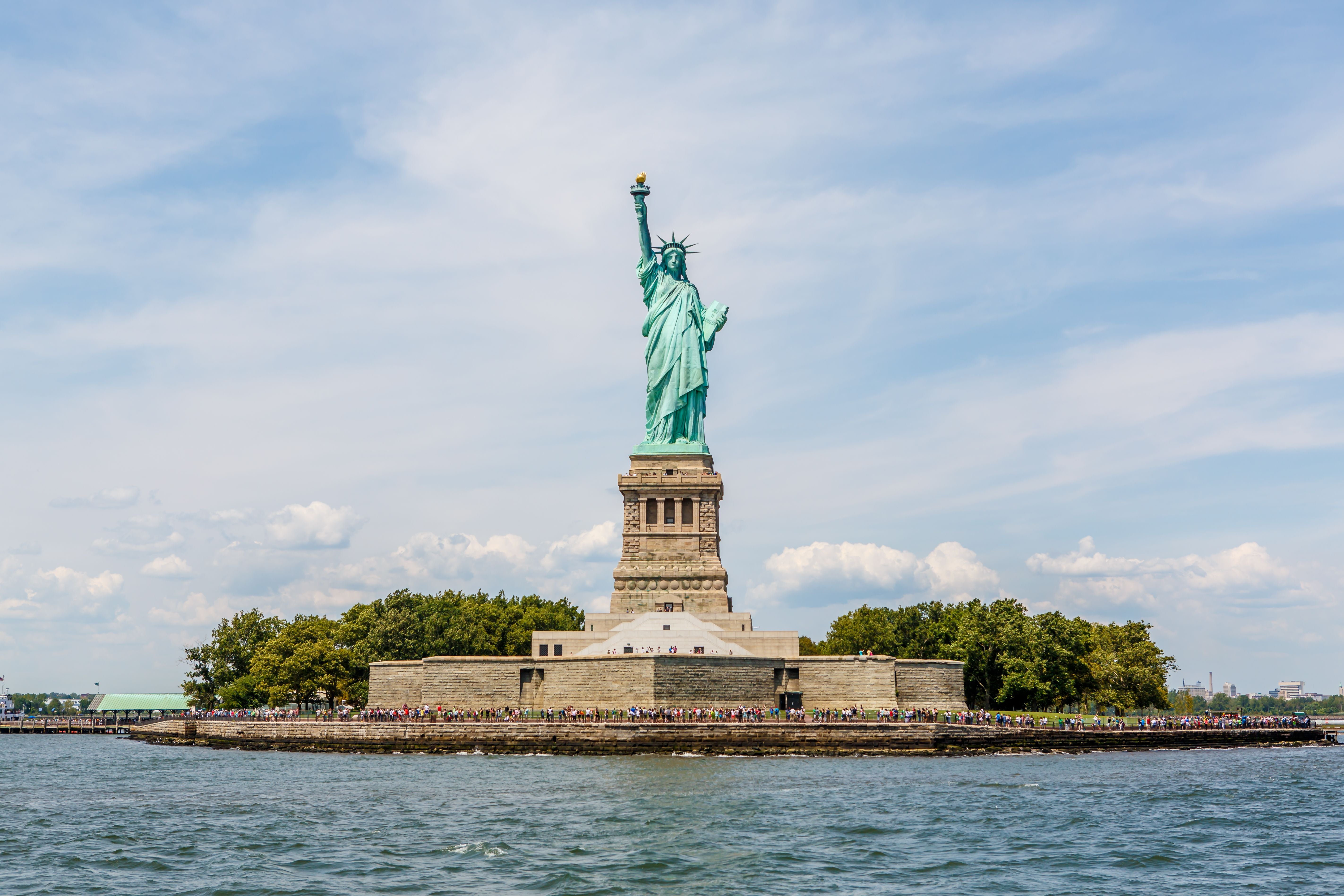 Die Freiheitsstatue steht auf Liberty Island im Hafen von New York unter blauem Himmel.