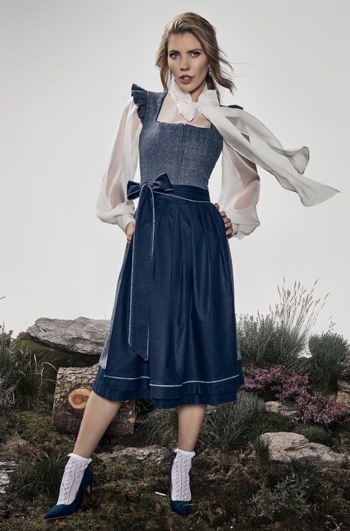 Frau trägt ein elegantes, dunkelblaues Dirndl mit weißer Bluse und Schleife im Freien.