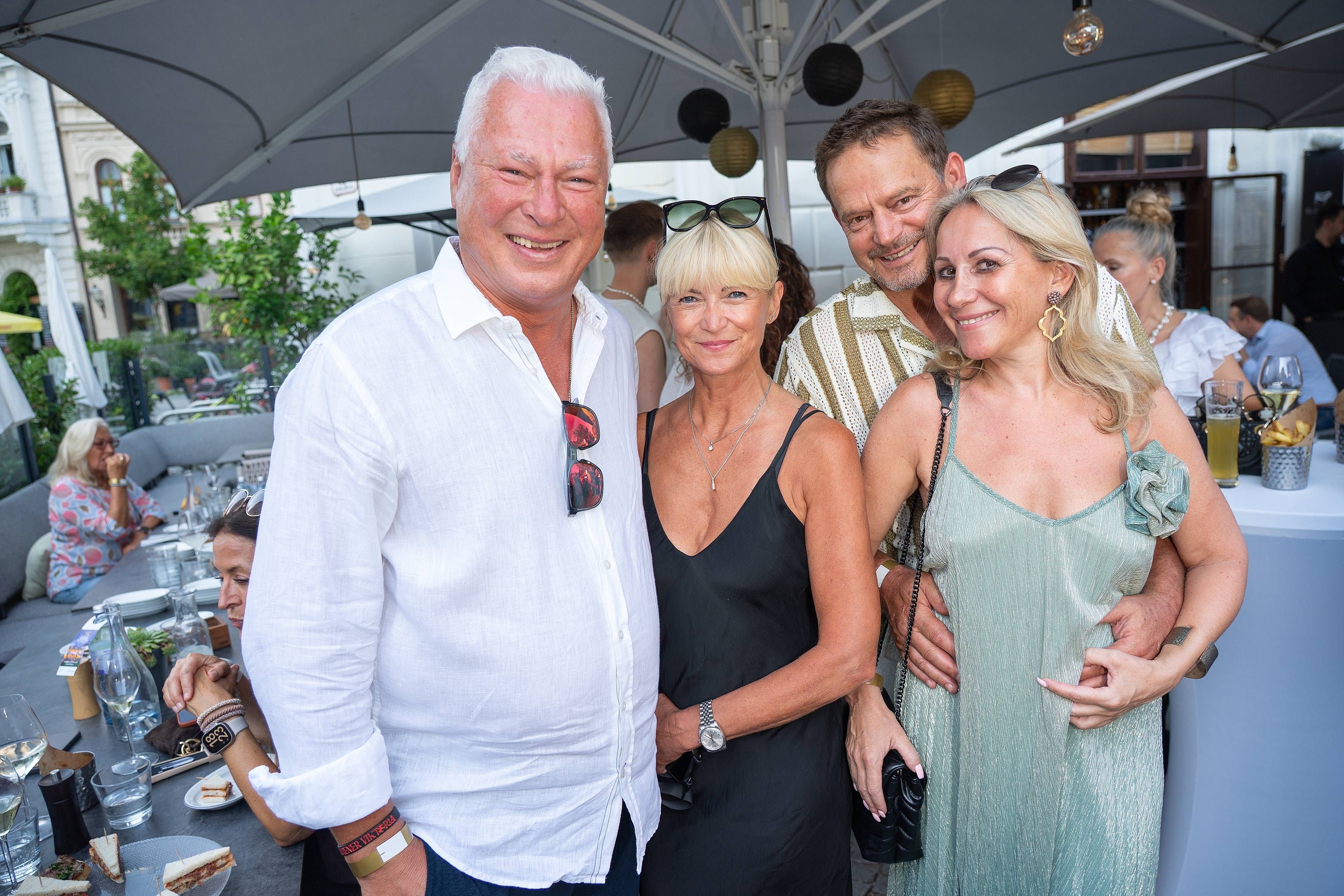 Vier fröhliche Erwachsene posieren bei einer Sommerfeier im Freien unter Sonnenschirmen.