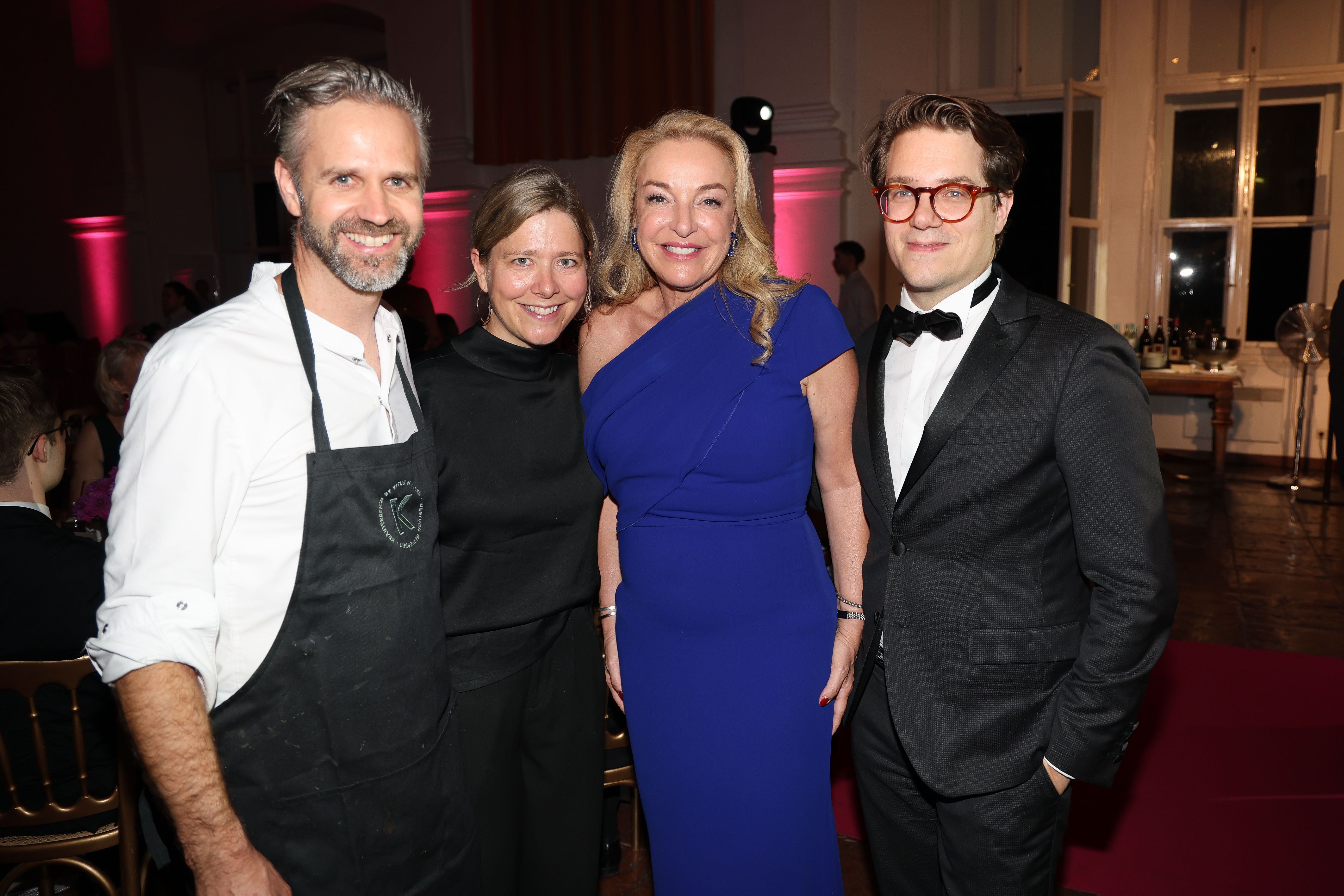 Vier elegant gekleidete Personen posieren bei einer Gala vor festlichem Hintergrund.