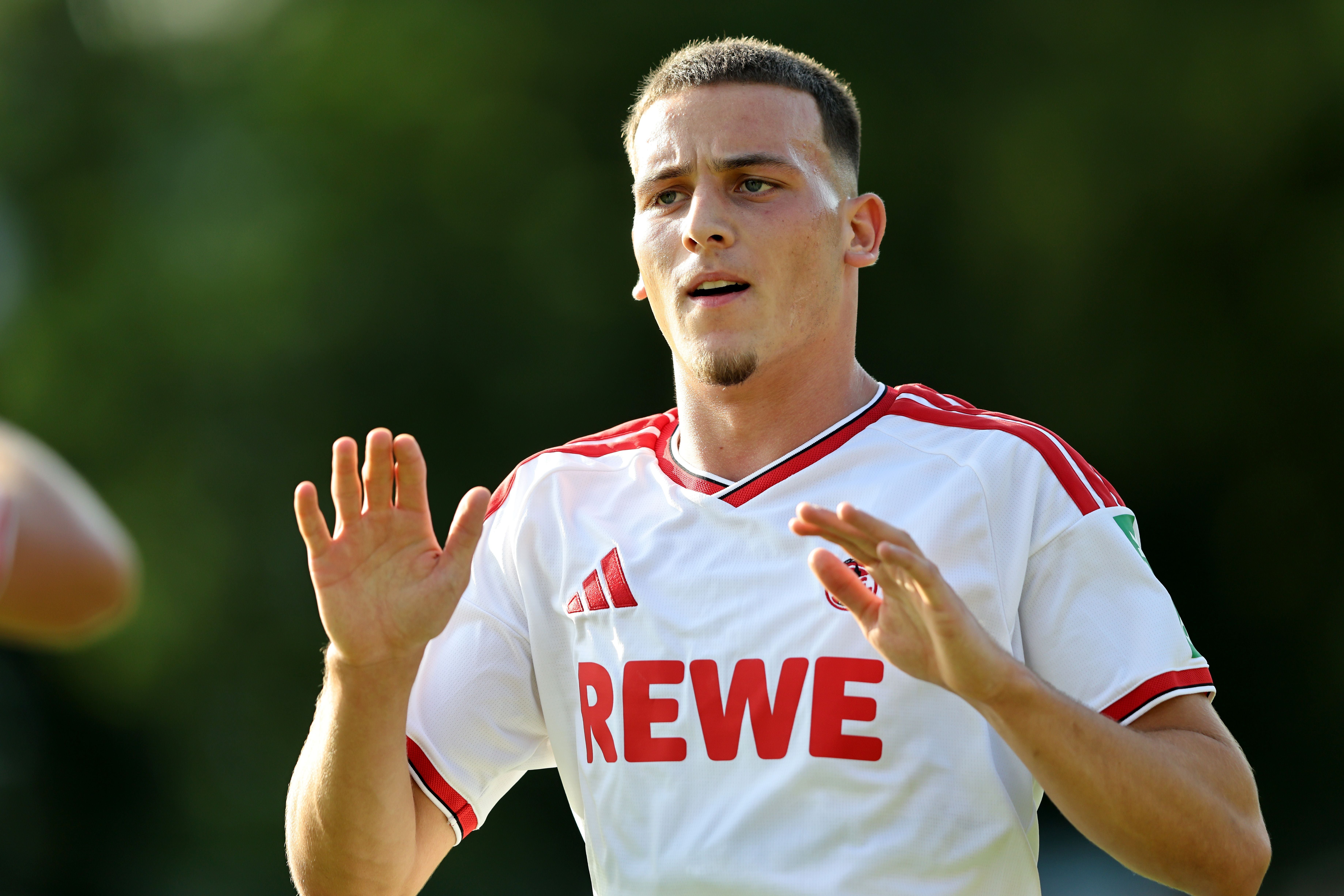 Ein Fußballspieler im weißen Trikot von 1. FC Köln jubelt mit erhobenen Händen auf dem Spielfeld.