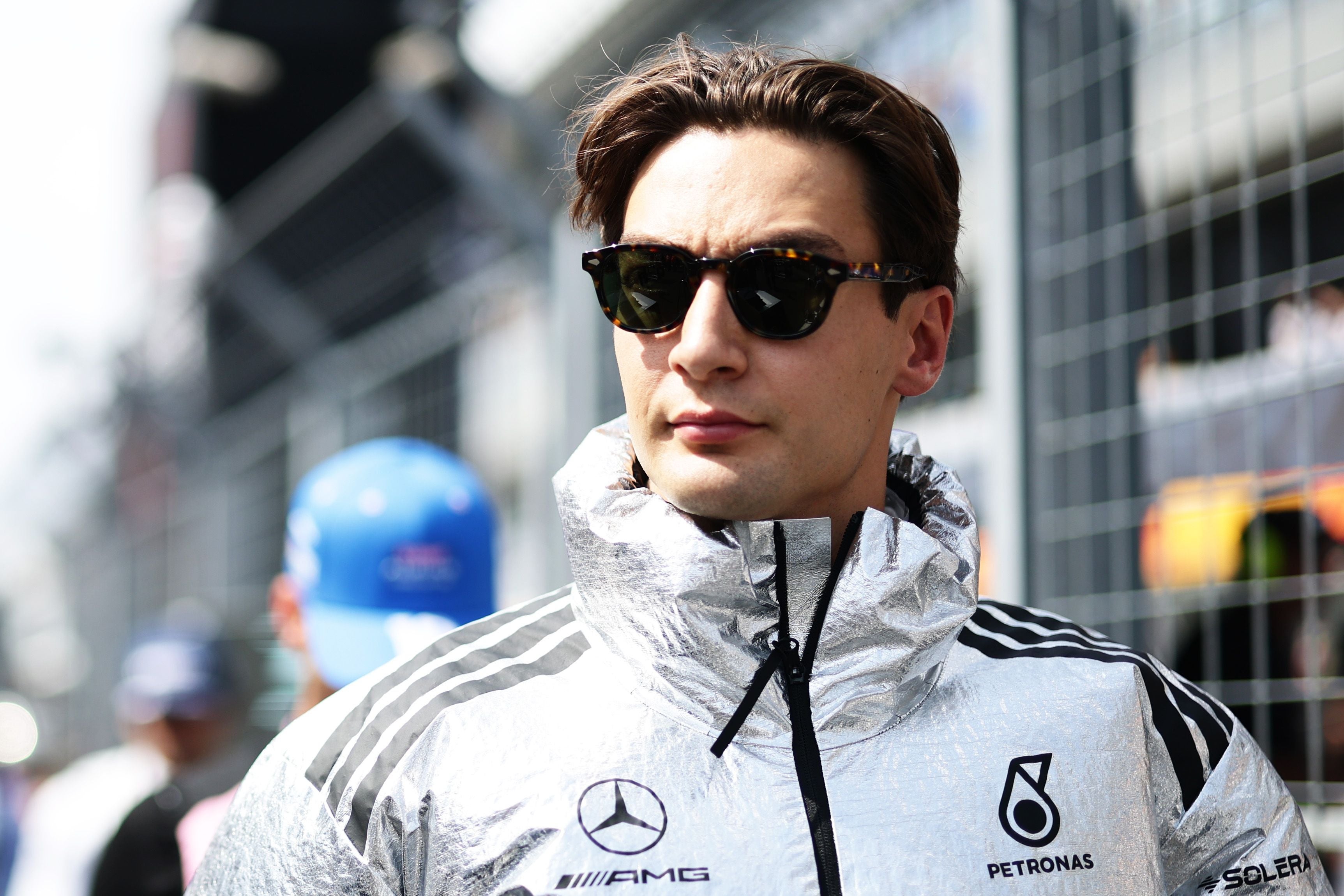 Ein Mann in silberner Mercedes-AMG-Jacke und Sonnenbrille steht auf einer Rennstrecke.