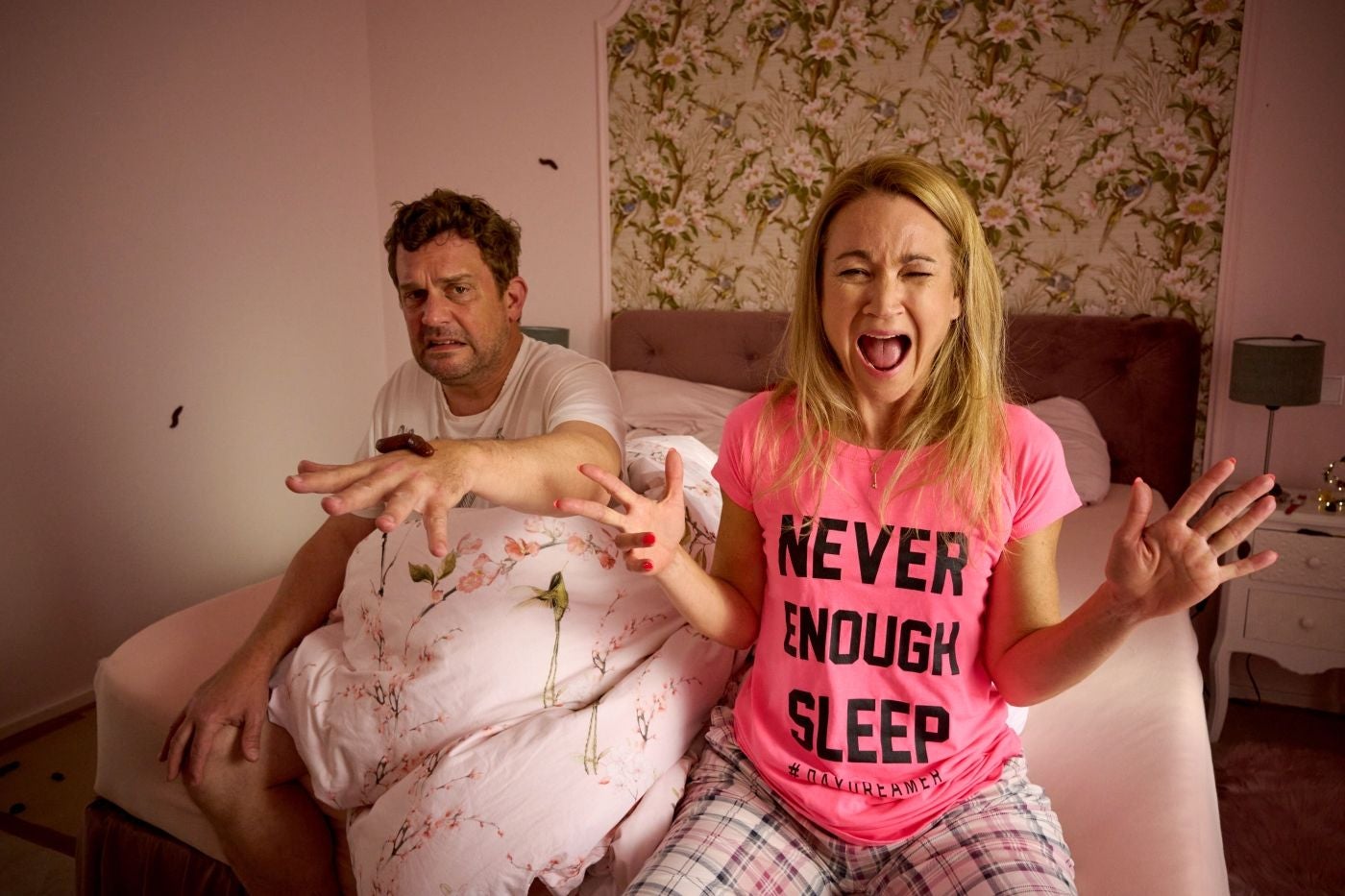 Mann und Frau im Bett erschrecken sich vor Kakerlaken im Schlafzimmer.