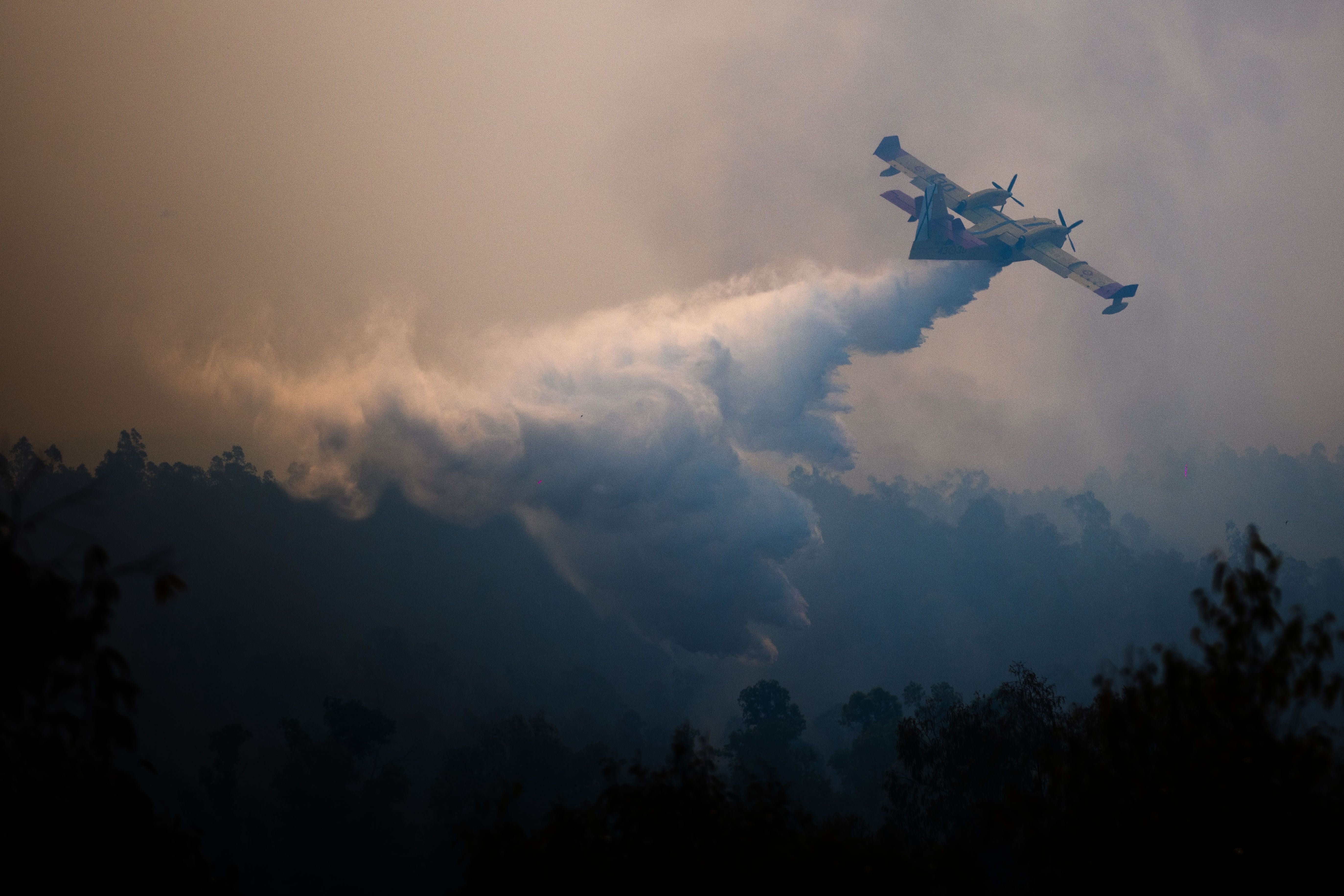 Ein Löschflugzeug wirft Wasser über einen brennenden, von Rauch bedeckten Wald ab.