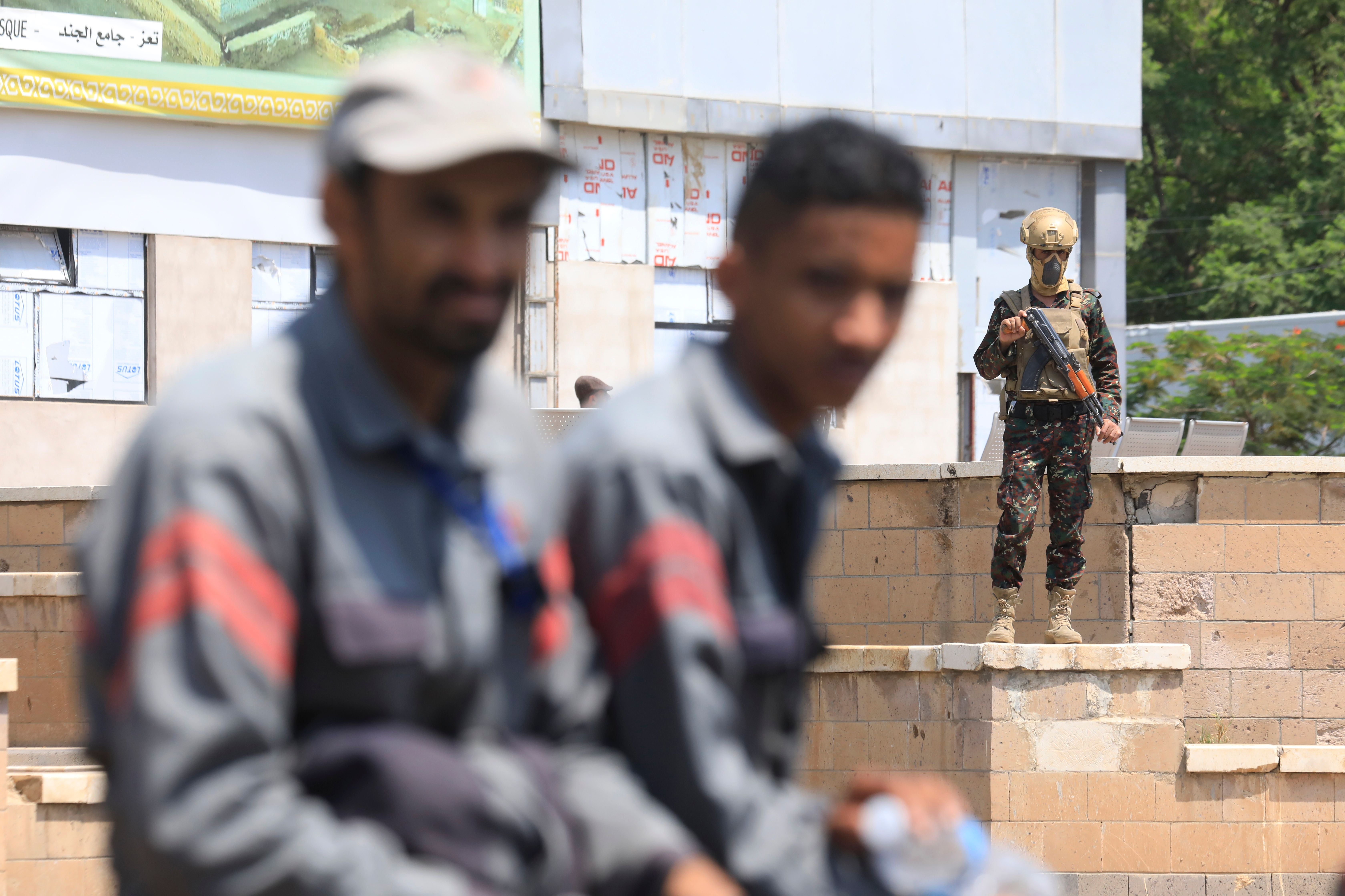 Ein Huthi-Soldat mit Gewehr steht Wache in der Nähe des Flughafens von Sanaa, unscharfe Männer im Vordergrund.