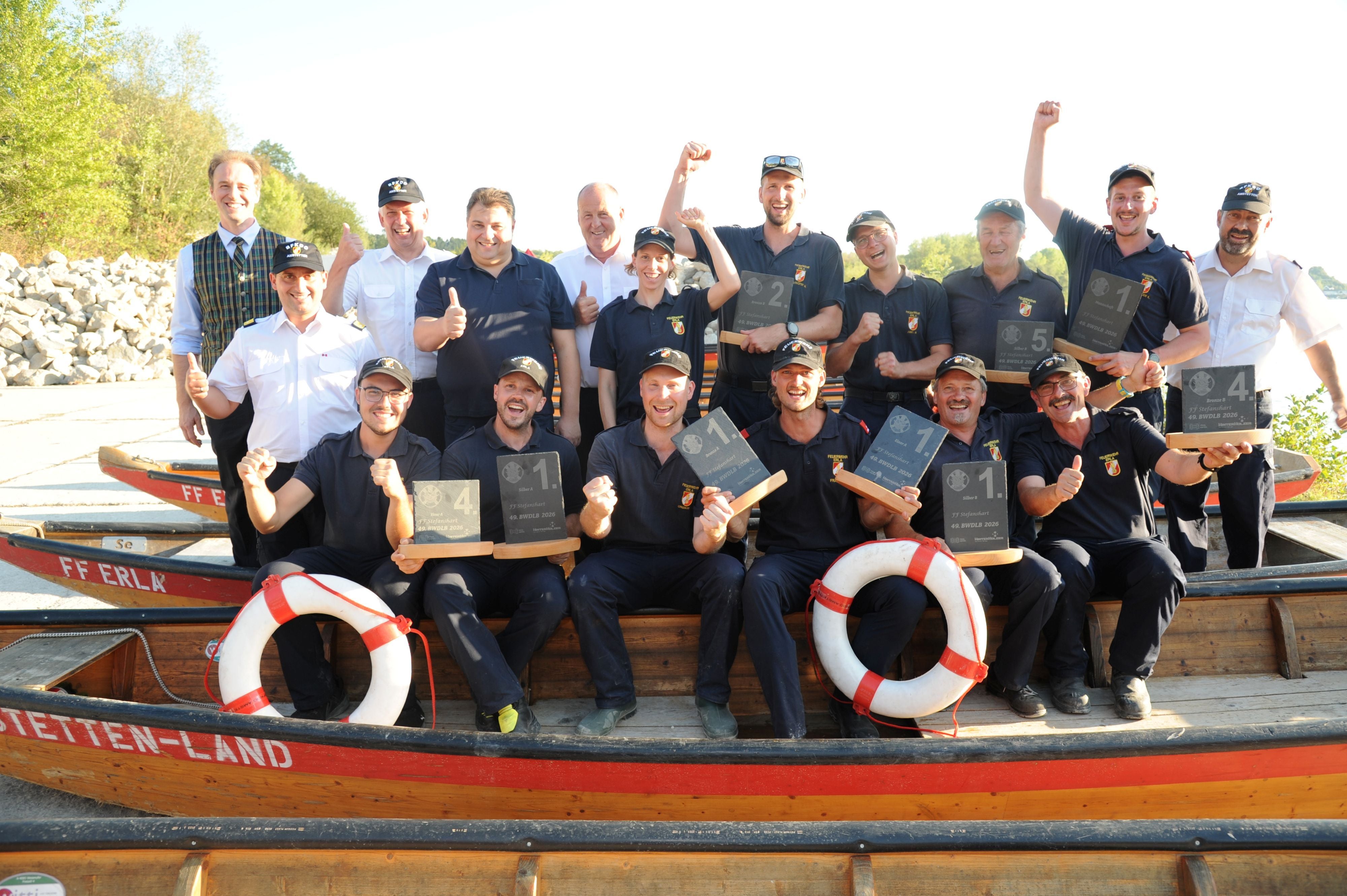 Eine Gruppe Männer posiert auf Booten mit Trophäen und Rettungsringen, jubelt und lächelt.