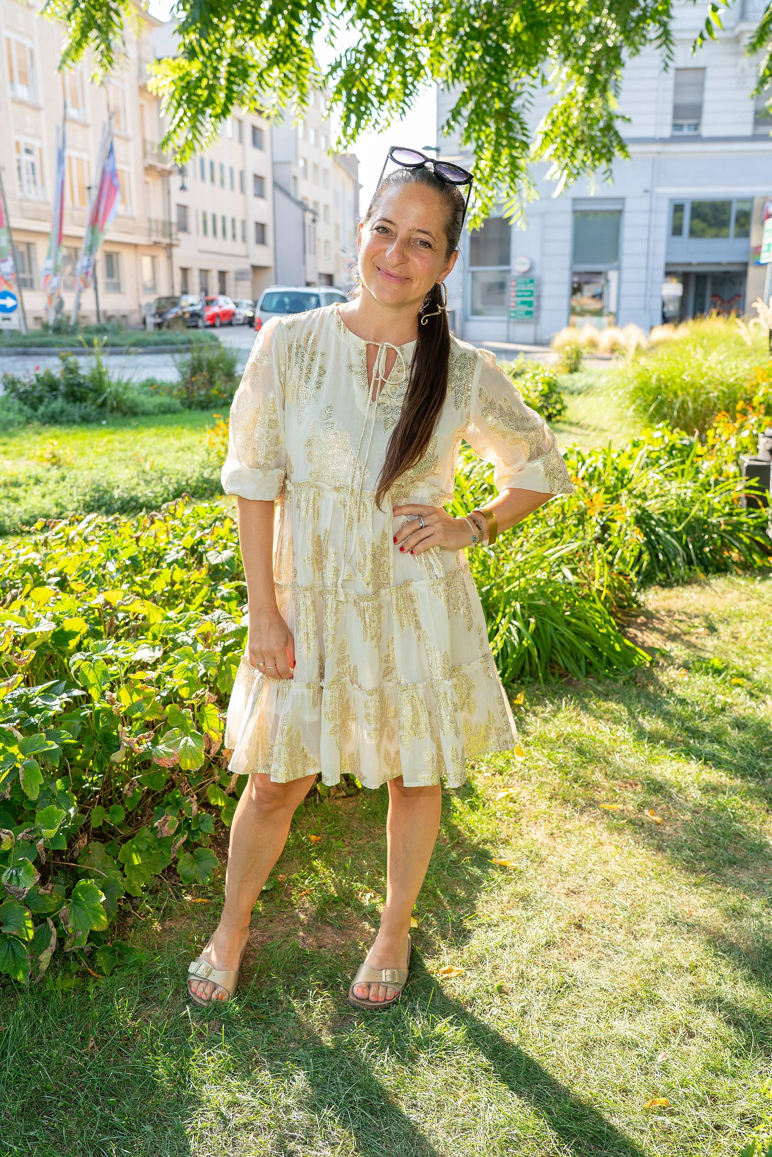 Frau im hellen Sommerkleid steht lächelnd im sonnigen Park bei einem Sommerfest.