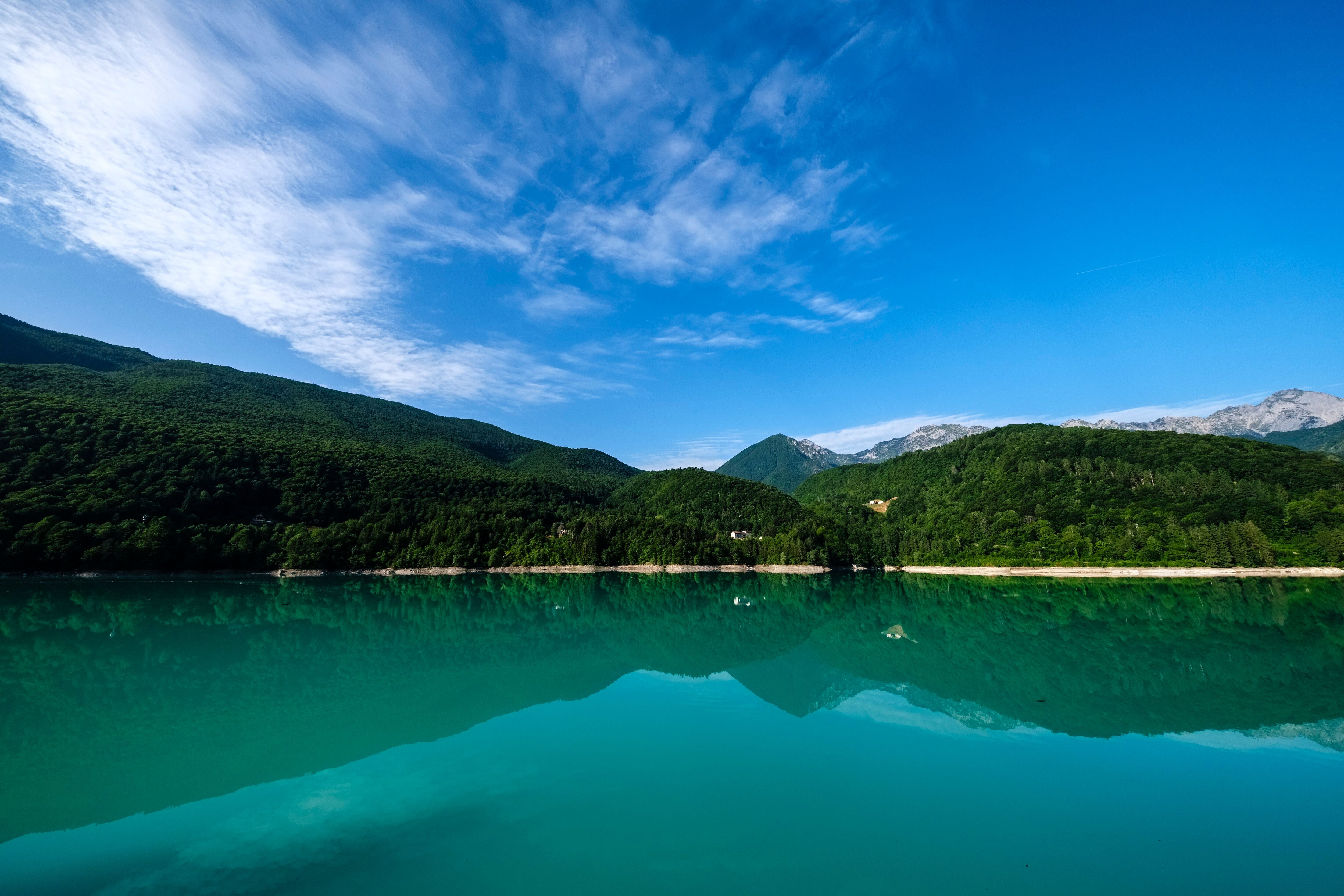 Türkisfarbenes Wasser des Lago di Barcis mit bewaldeten Bergen und blauem Himmel im Hintergrund.