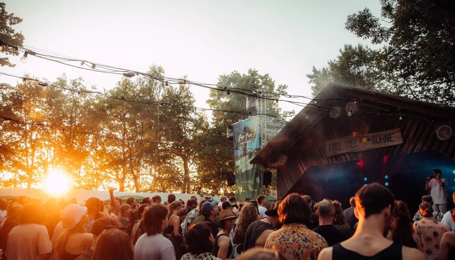 Menschenmenge vor einer Bühne im Freien beim Free Tree Open Air bei Sonnenuntergang.