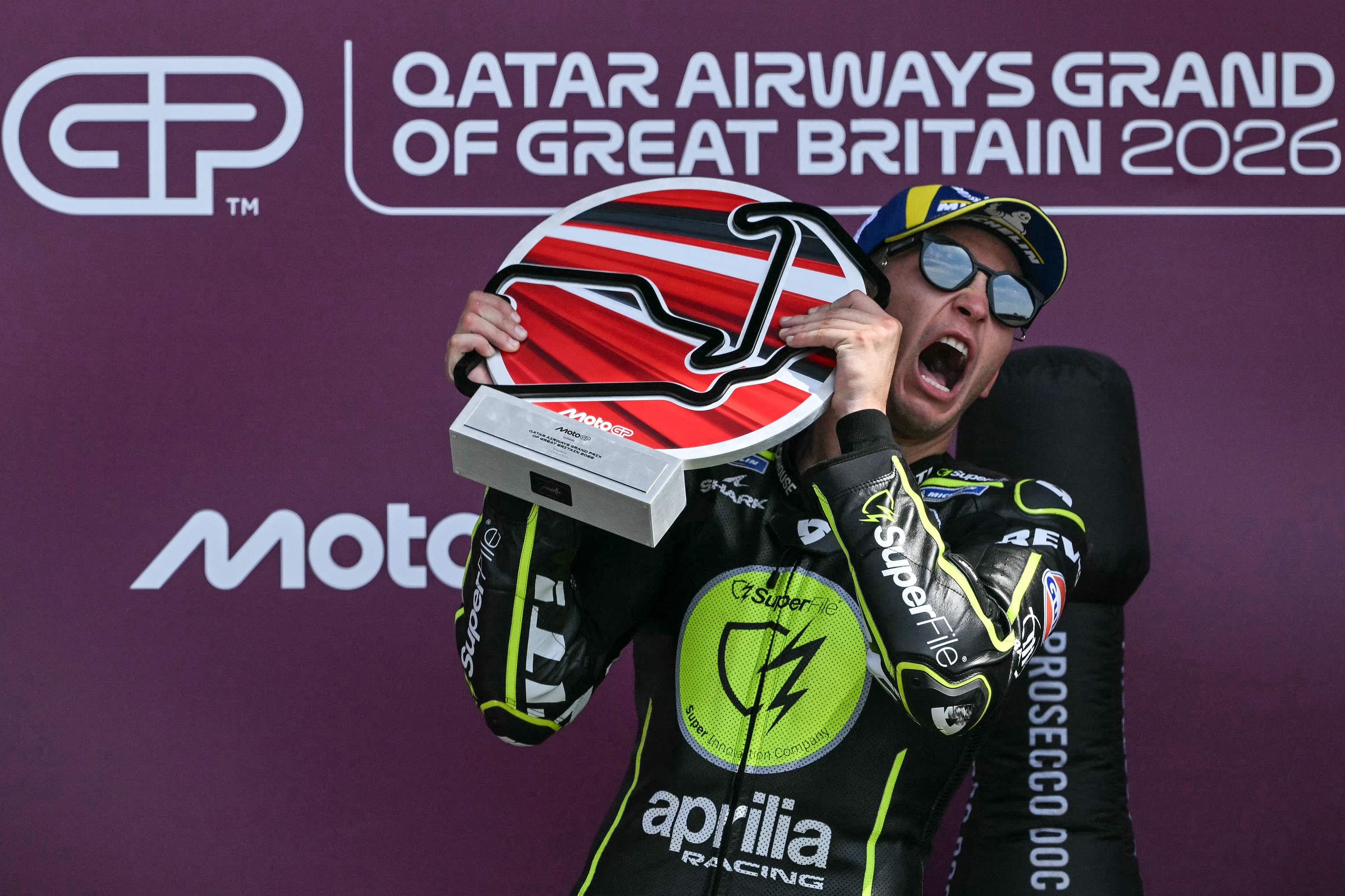 Ein Motorradrennfahrer jubelt mit einem großen Pokal auf dem Siegerpodest in Silverstone.