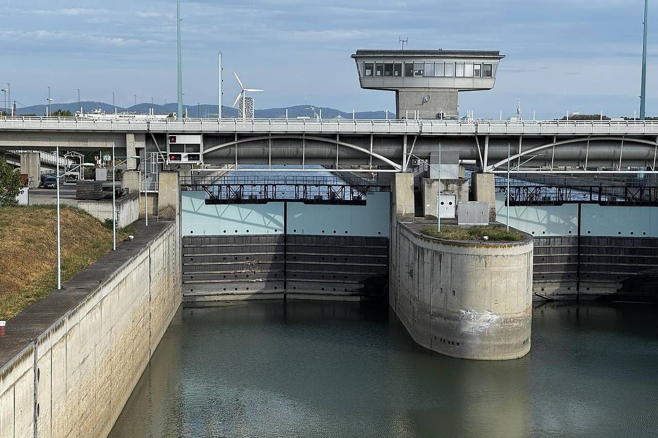 Schleuse mit geschlossenen Toren und Steuerhaus, Brücke und Windrad im Hintergrund.