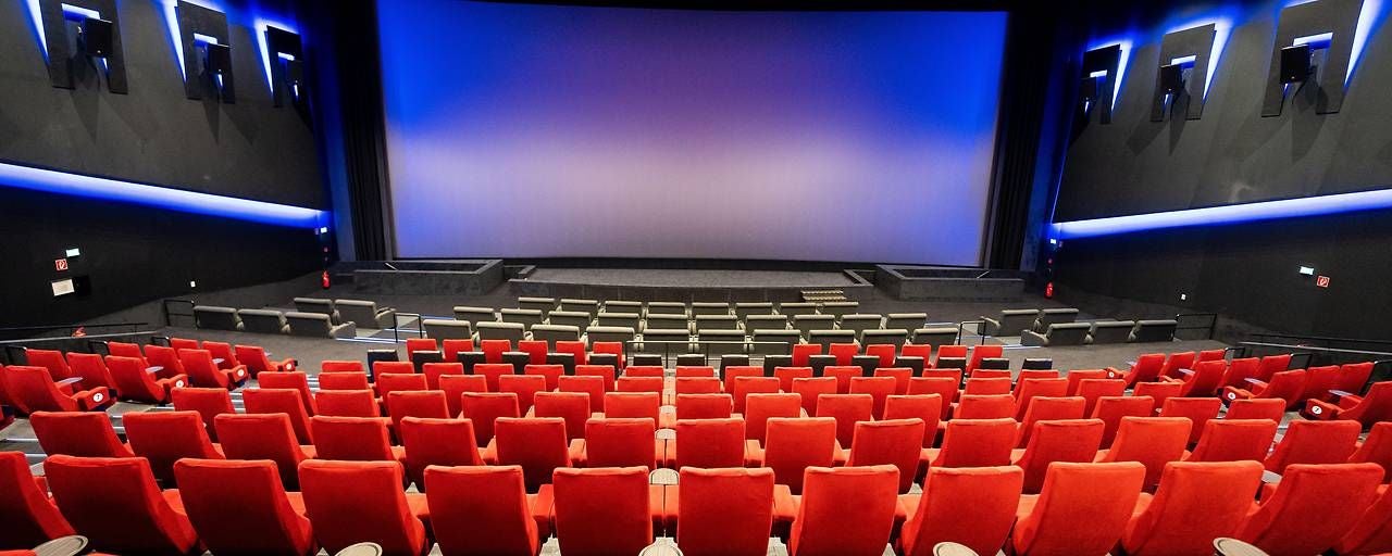 Modernes Kino mit roten Sitzen, leerem Saal und großer Leinwand vorne.