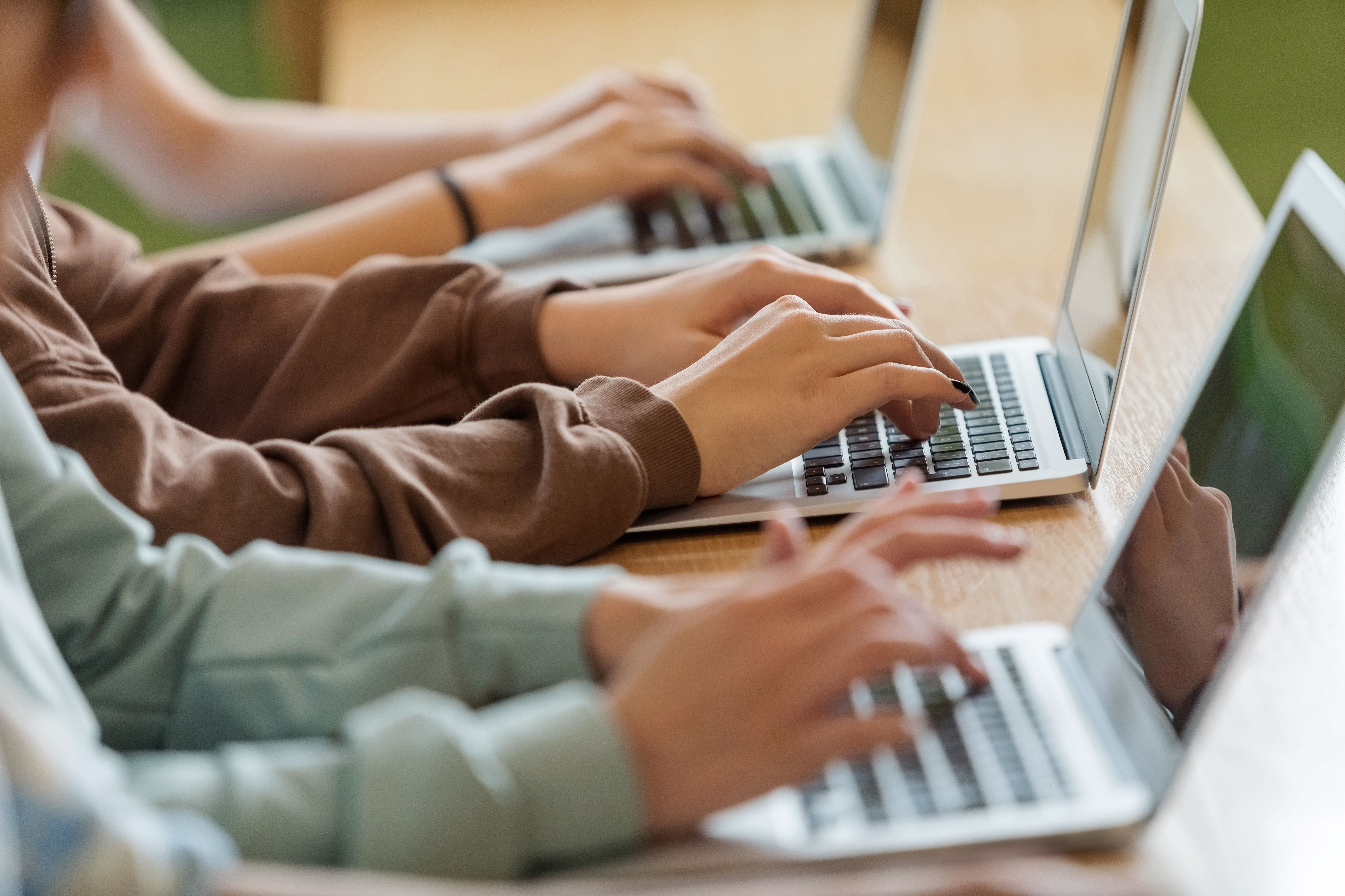 Hände von Schülern tippen im Klassenzimmer während des Unterrichts auf Laptops.