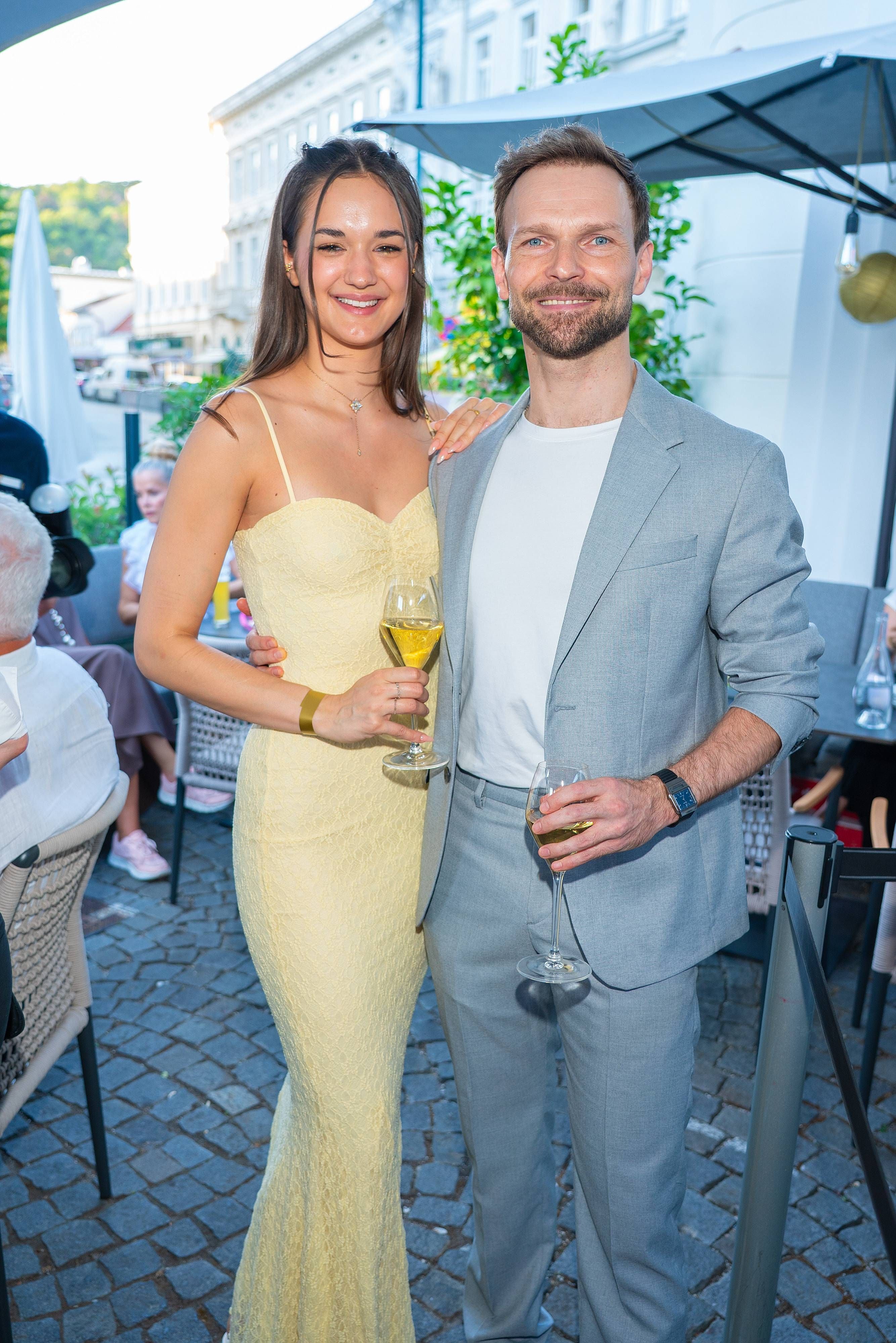 Ein junges Paar feiert draußen auf einer Sommerparty mit Weingläsern in der Hand.