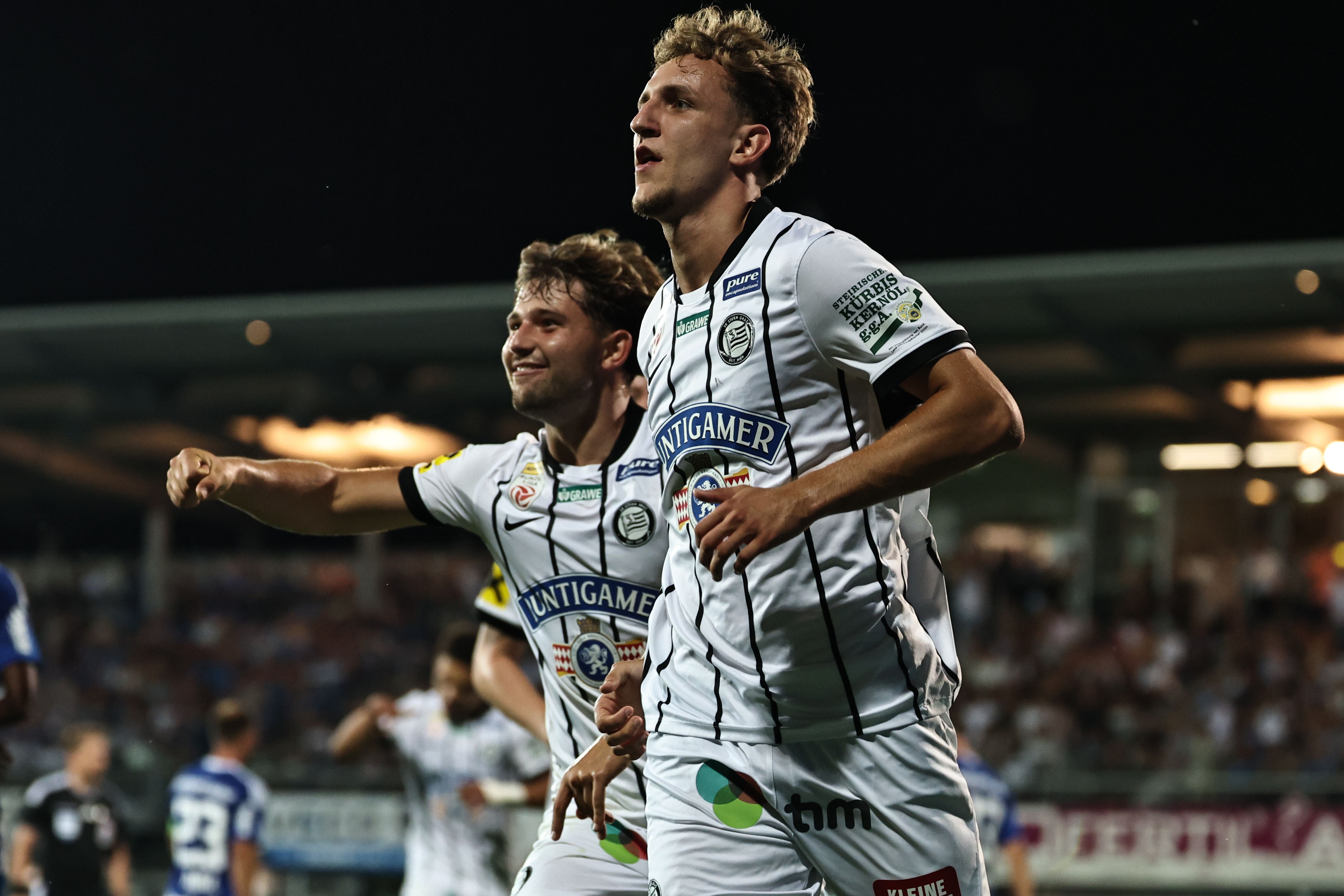 Zwei Fußballspieler von Sturm Graz jubeln im Stadion nach einem Tor.
