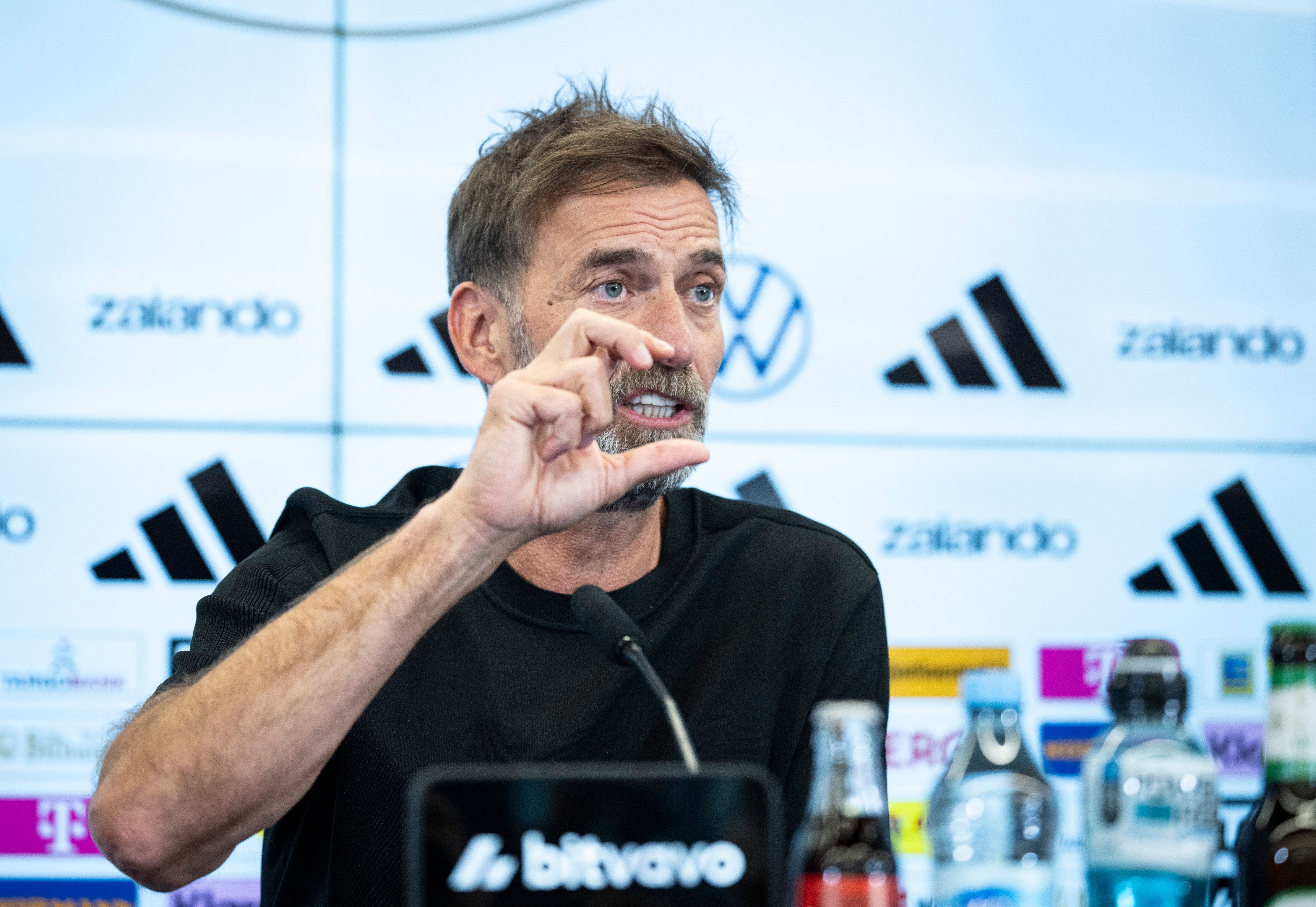 Ein Mann spricht auf einer Pressekonferenz und zeigt mit den Fingern eine kleine Größe an.