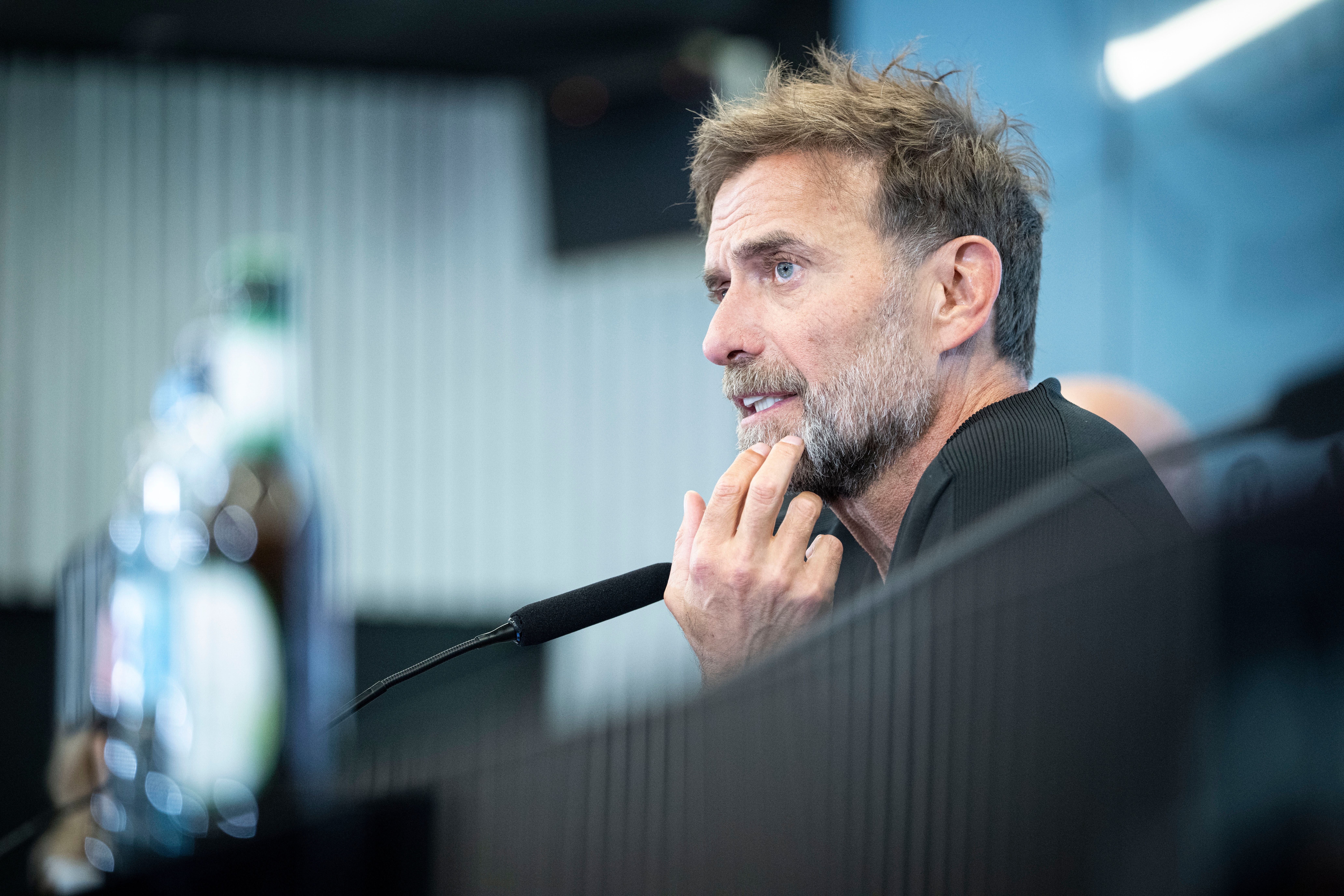 Ein Mann mit Bart spricht nachdenklich in ein Mikrofon bei einer Pressekonferenz.
