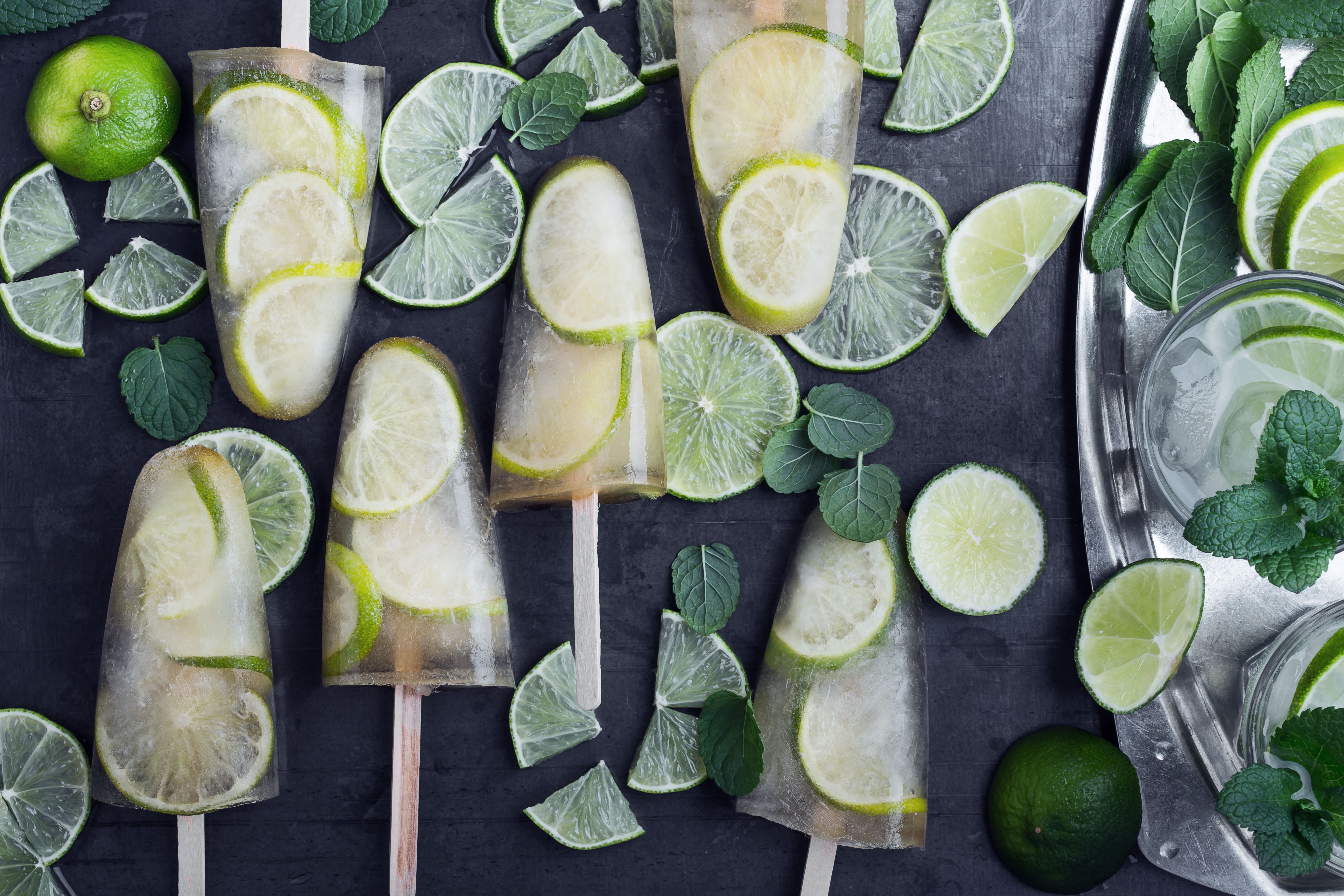 Gefrorene Mojito-Eis am Stiel mit Limettenscheiben und frischer Minze auf dunklem Hintergrund.