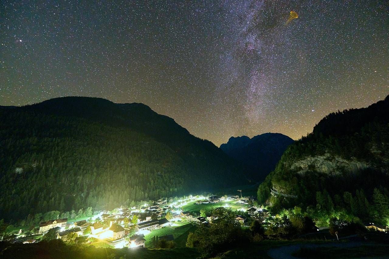 Ein Dorf im Naturpark Weißbach bei Nacht, umgeben von Bergen und funkelndem Sternenhimmel.