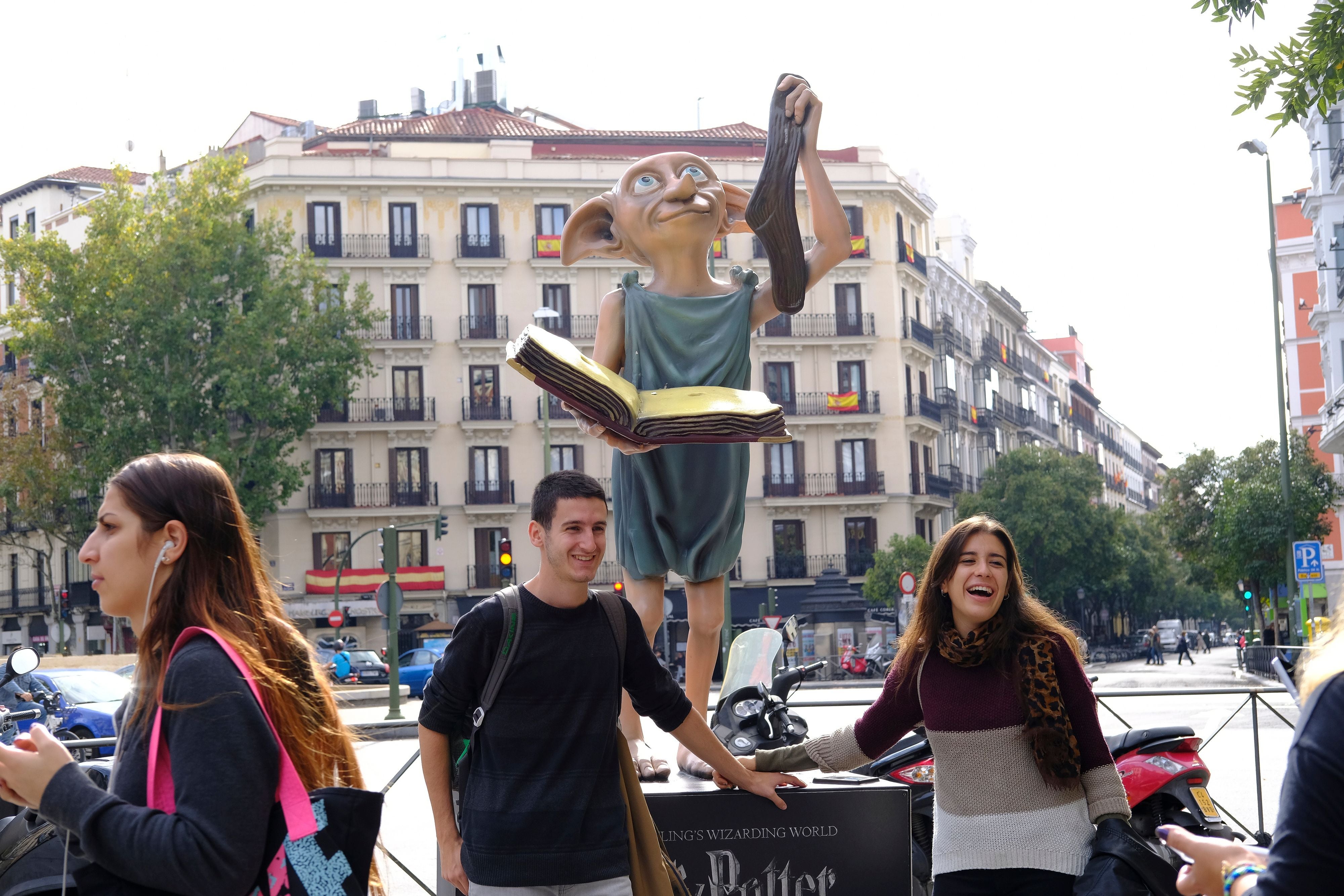 Statue von Dobby mit Buch in der Hand, umgeben von lachenden jungen Menschen in Madrid.
