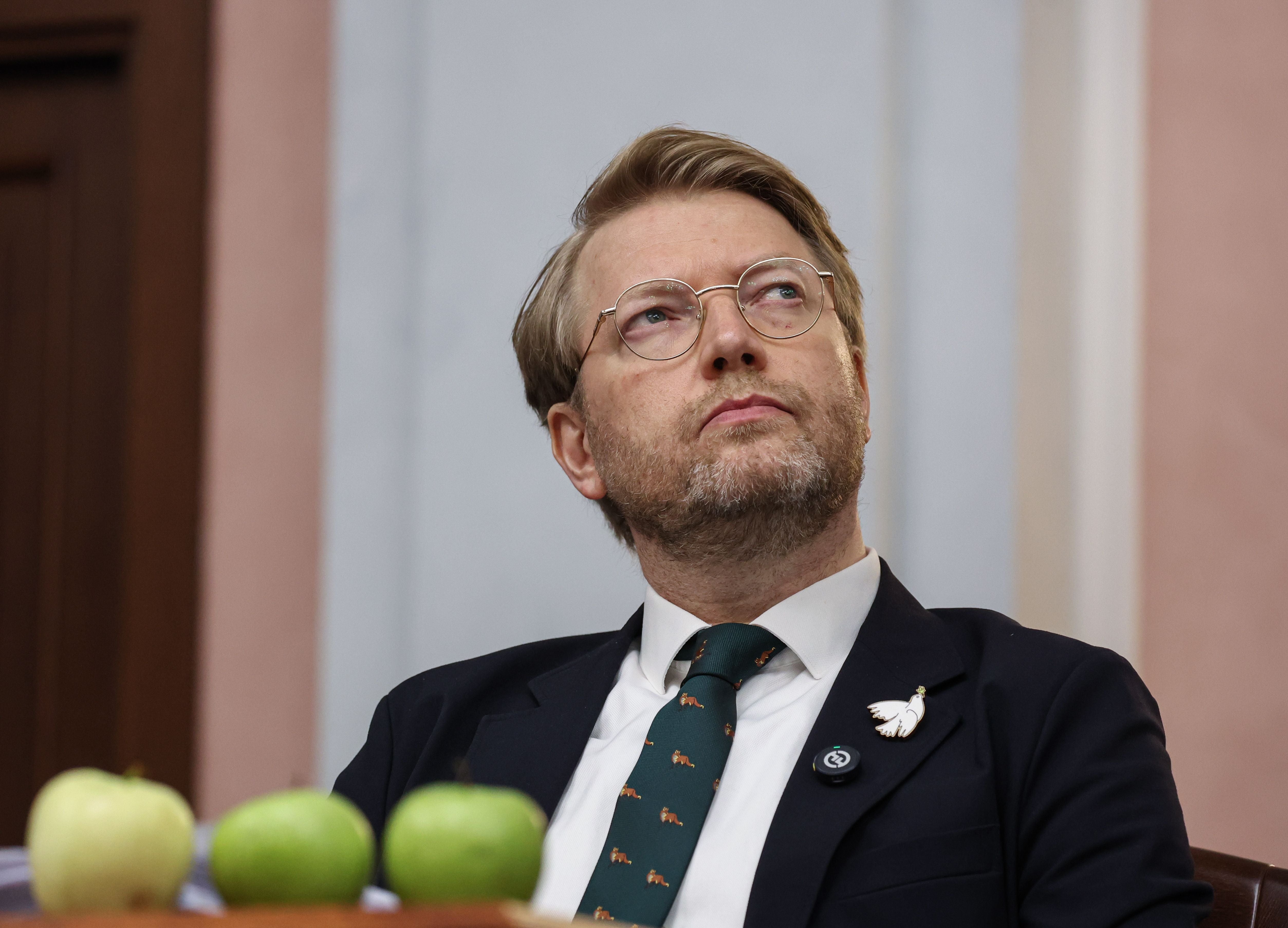 Der Vorsitzende der russischen Jabloko-Partei, Nikolai Rybakow mit Brille und Anzug sitzt nachdenklich, vor ihm liegen mehrere grüne Äpfel.