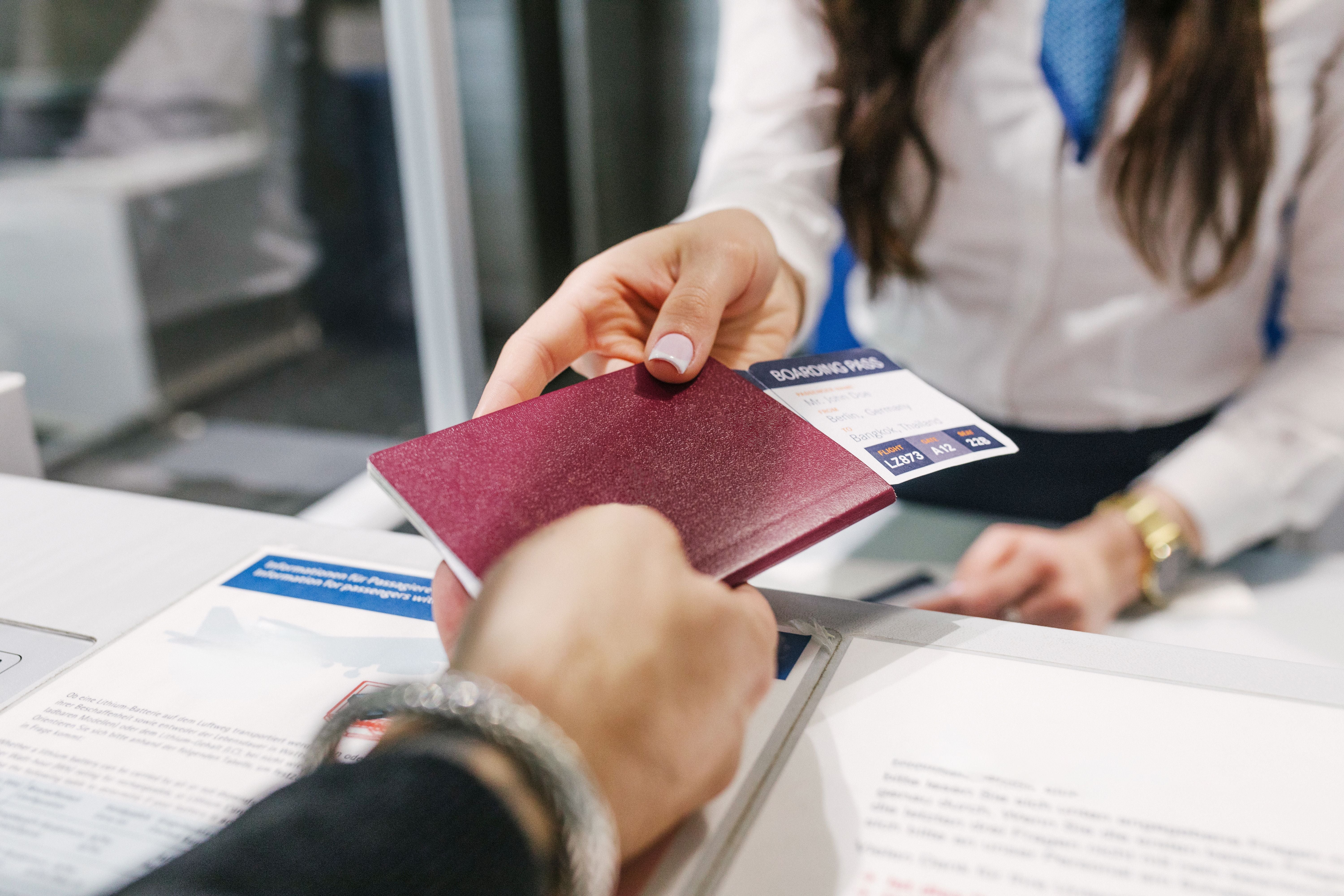 Nahaufnahme: Eine Person übergibt Reisepass und Bordkarte an eine Flughafenmitarbeiterin.