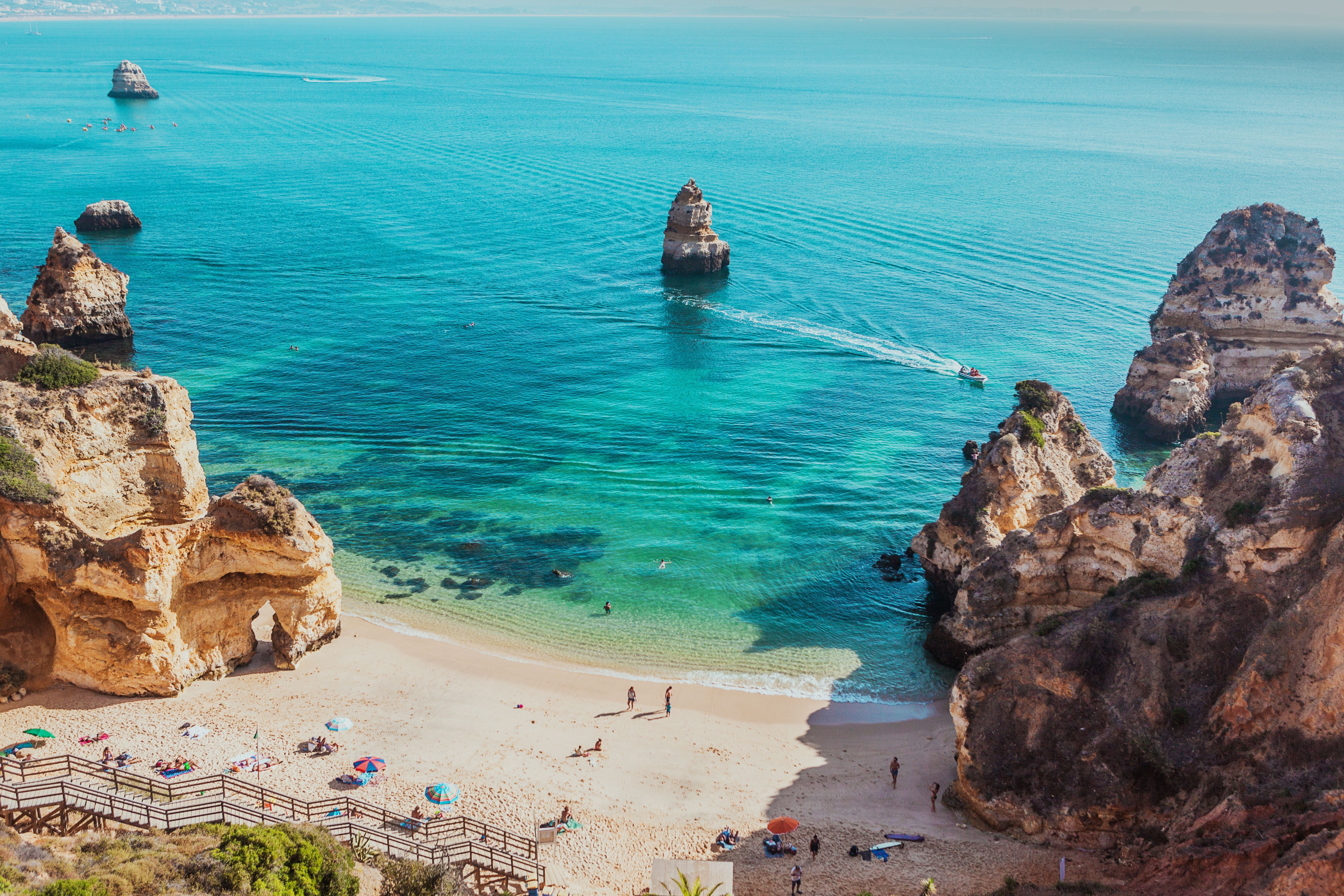 Sandstrand mit bunten Sonnenschirmen, umgeben von Felsen und türkisblauem Meer in Lagos, Algarve.