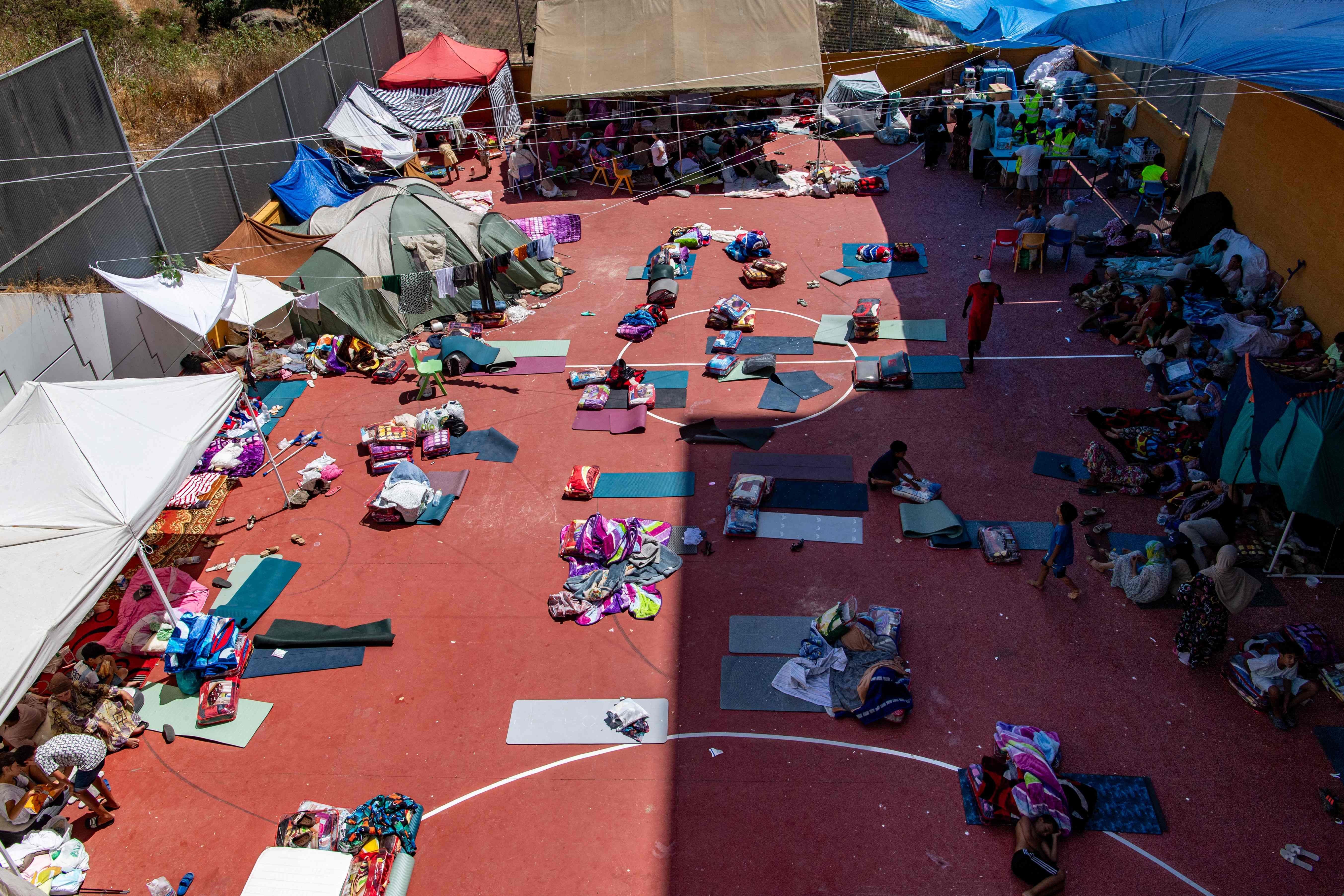 Migranten lagern mit Decken und Matten auf einem Sportplatz, teils unter Zelten und Planen in Ceuta.